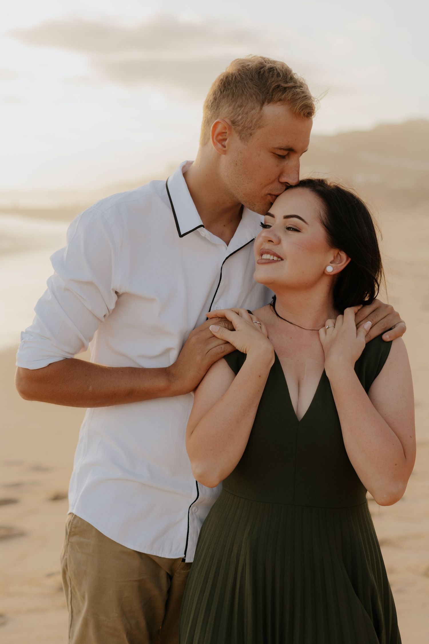 Man in white shirt kissing woman on forehead during golden hour Garden Route engagement photo session.