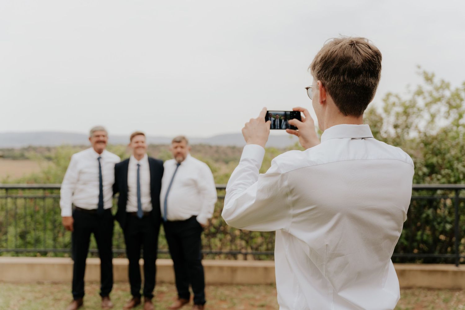 Wedding party members posing against a scenic rural landscape backdrop.