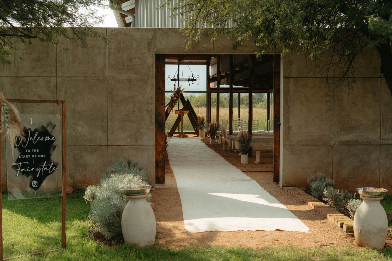 A rustic stone walkway entrance decorated with large clay pots and sage brush leading to an outdoor venue.