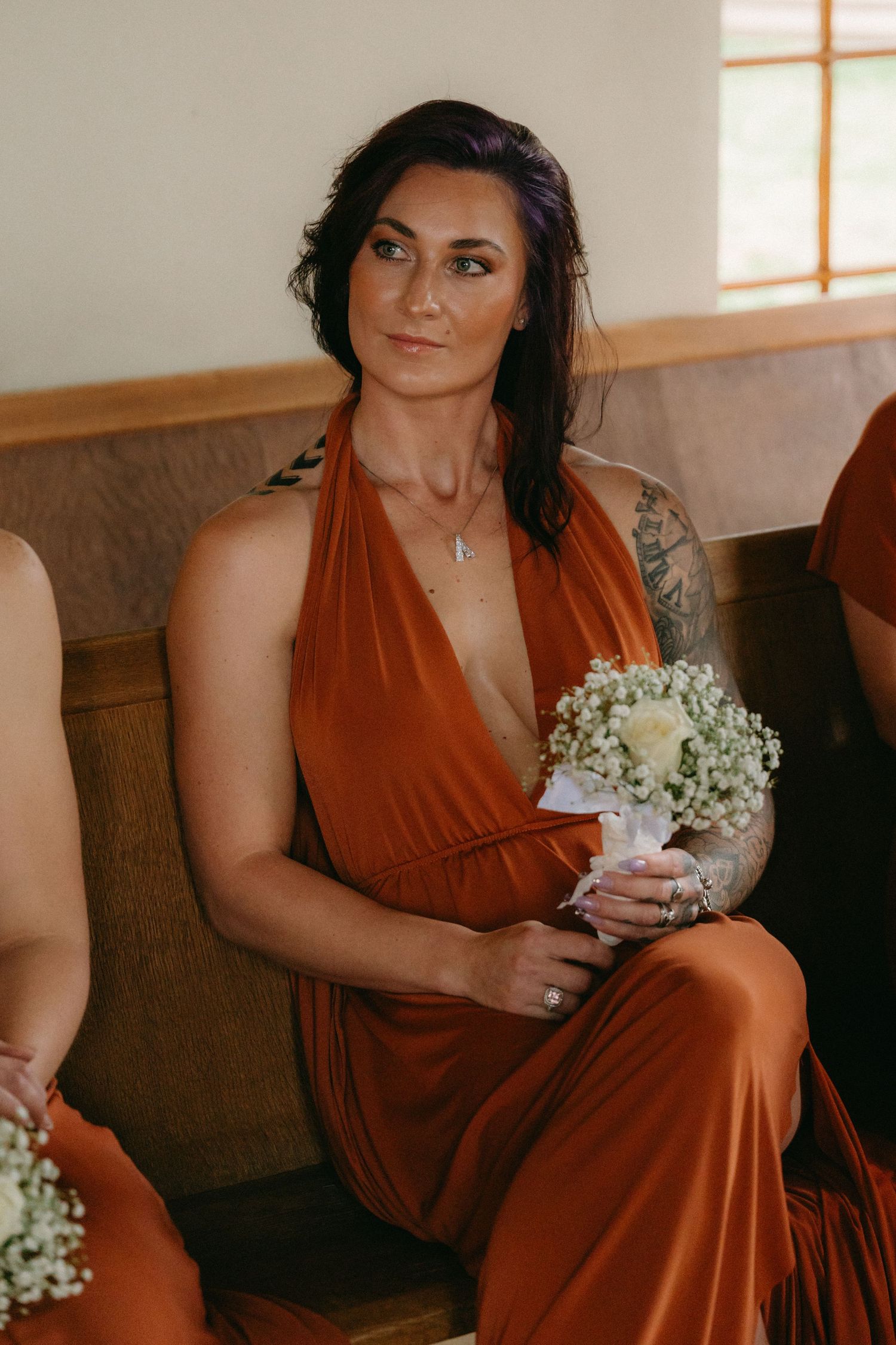 Bridesmaids in rust-colored dresses hold delicate white bouquets while seated indoors.