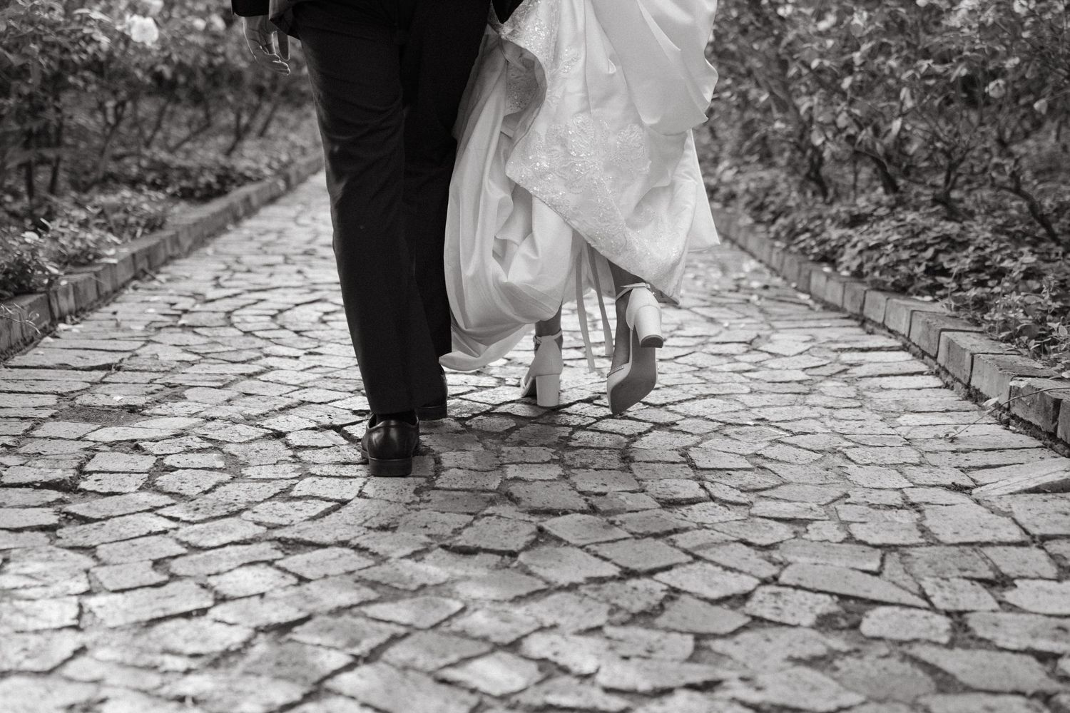 Black and white photo of wedding couple's feet walking together on a stone pathway.