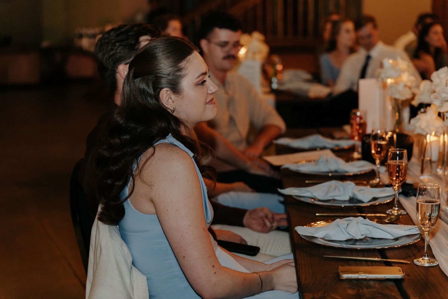 Wedding reception guests seated at elegant tables with candlelight and place settings.