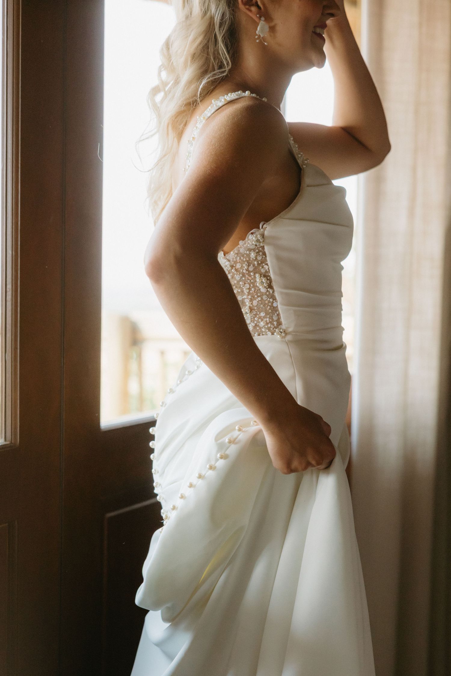Elegant white wedding dress detail shot near a window with natural lighting.