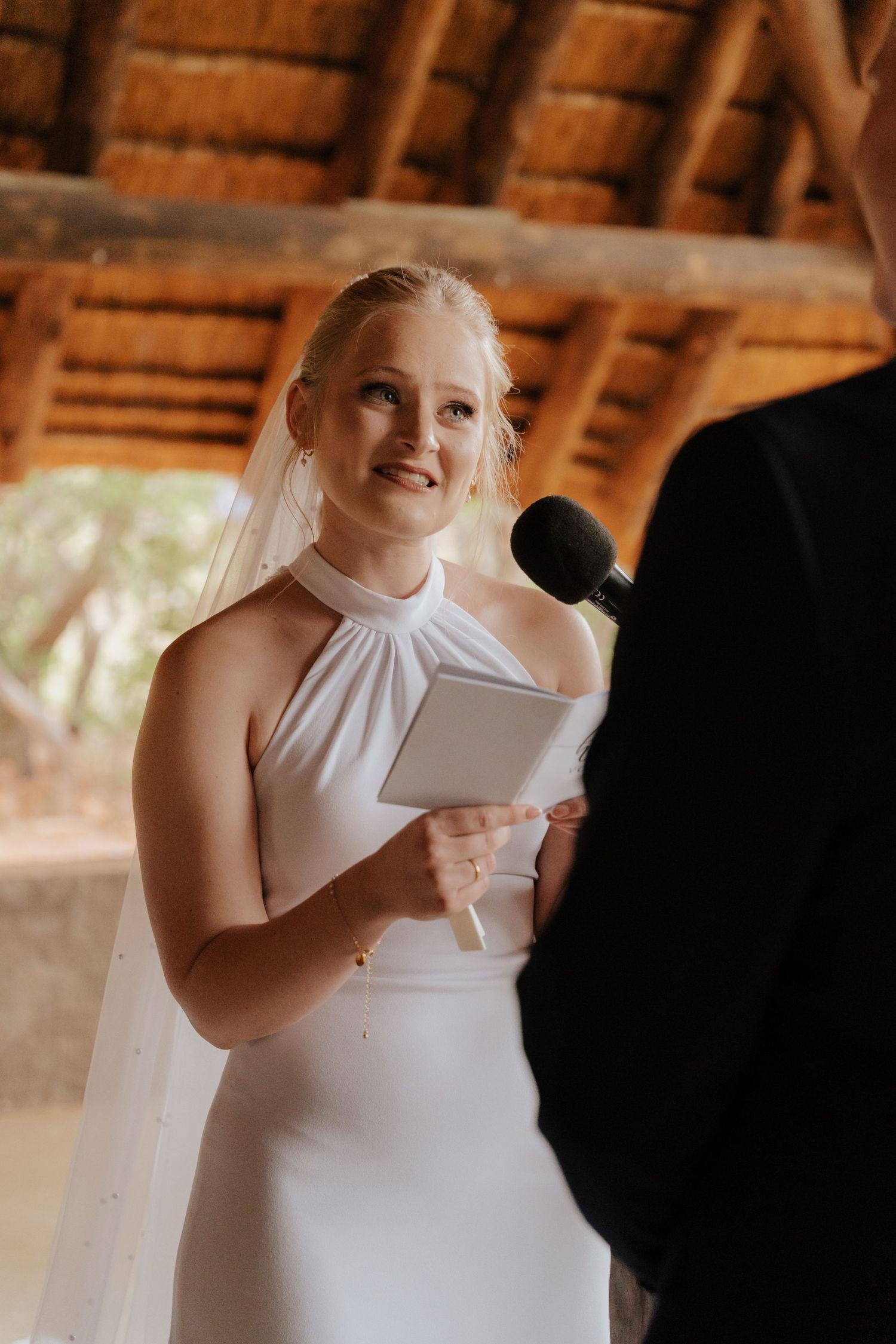 Close-up shots of a person in a white halter wedding dress smiling and holding papers during a ceremony.