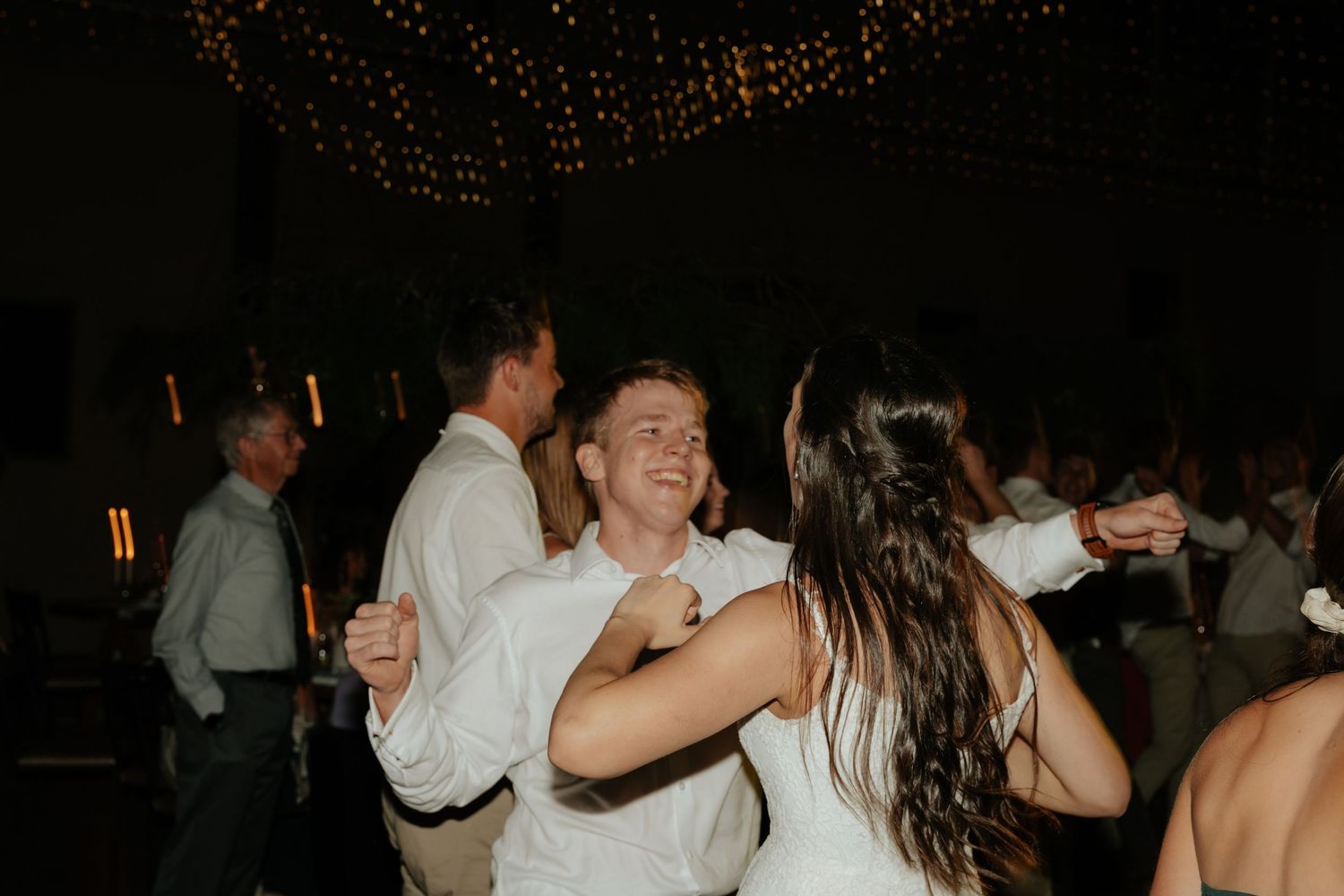 Wedding guests dancing and celebrating together on a dimly lit dance floor during an evening reception.