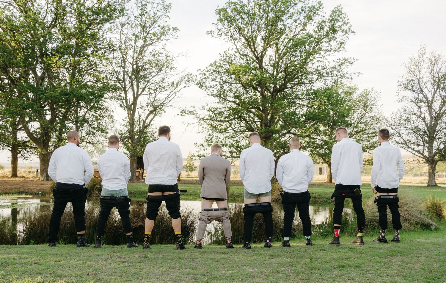 Eight people in white shirts and black shorts stand in a line overlooking a scenic golf course at sunset.
