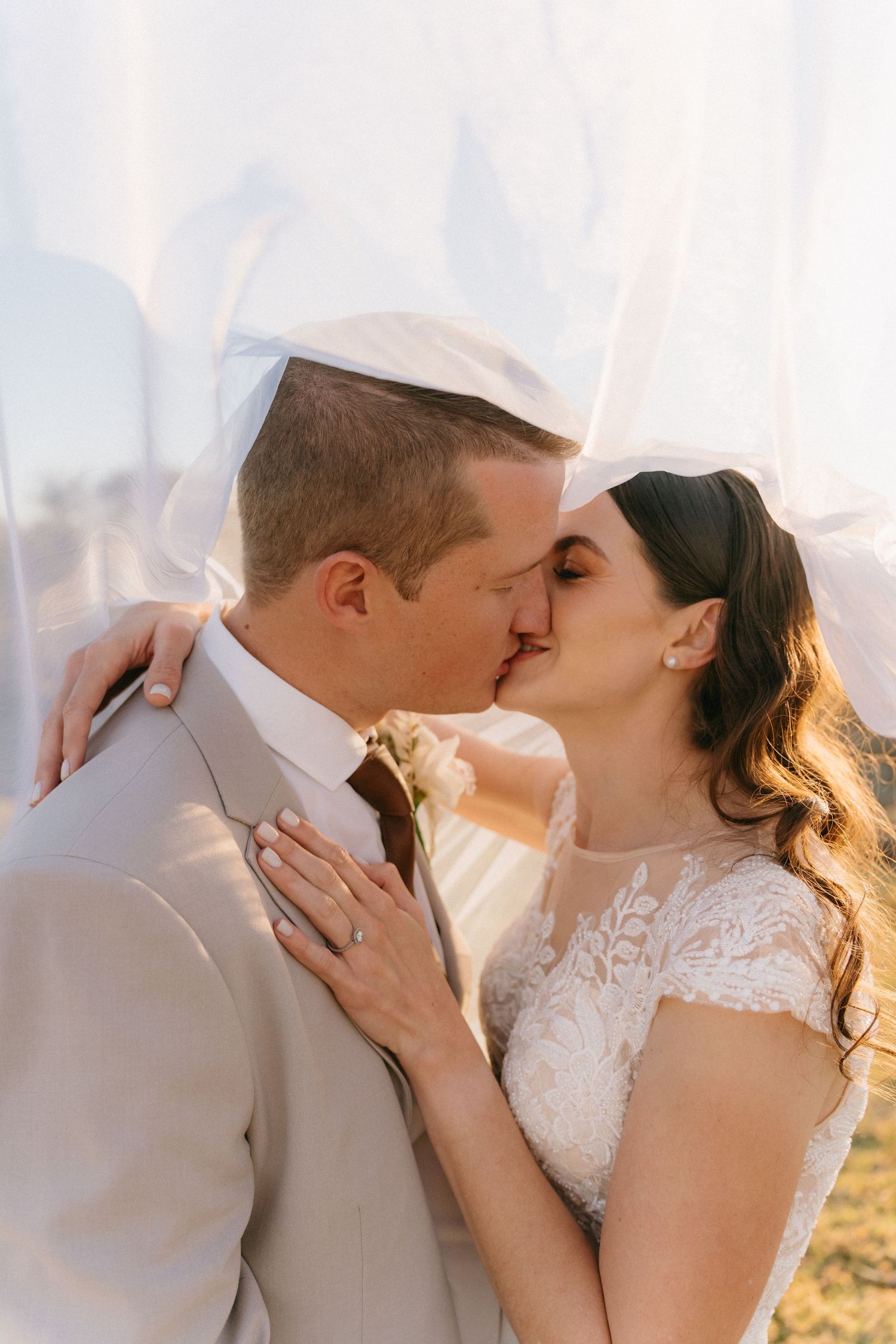 Romantic wedding couple sharing intimate kisses in golden sunlight against a soft background.