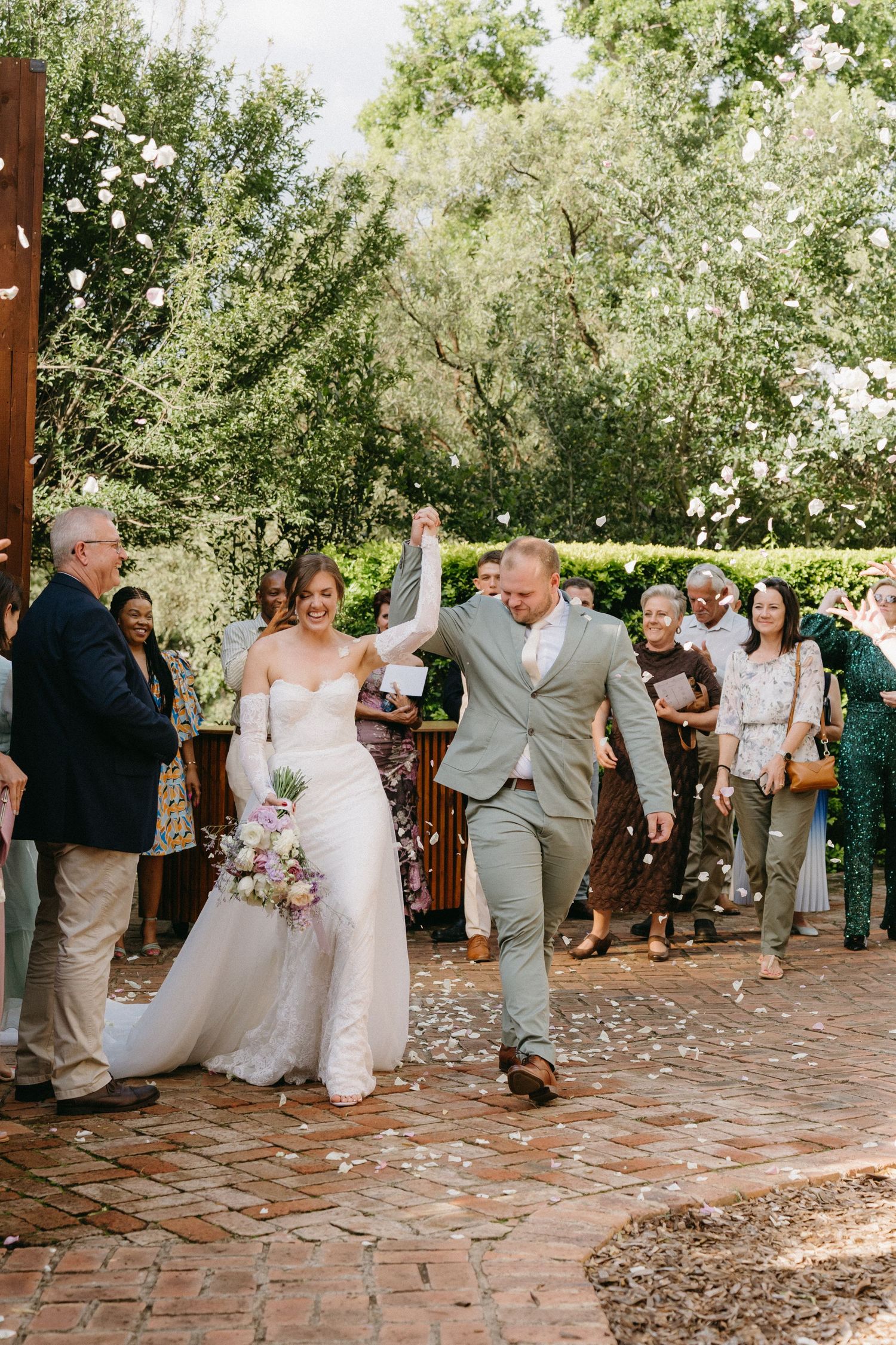 Newlyweds celebrate with joyful exit down brick pathway at outdoor garden wedding ceremony.