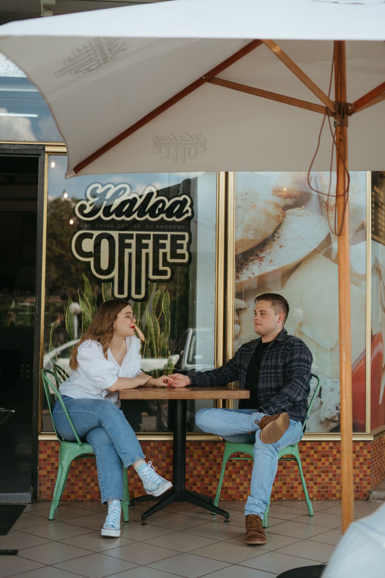 Customers enjoy conversation at an outdoor table under white umbrella at Haloa Coffee shop during daytime.
