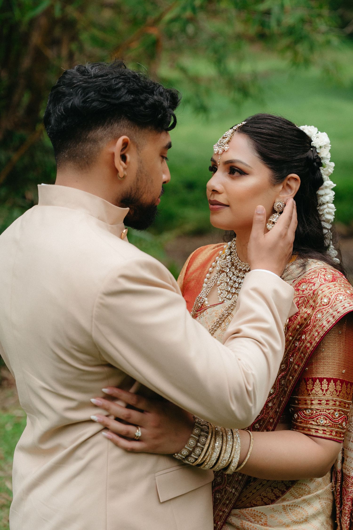 A couple in traditional South Asian wedding attire embraces romantically in a garden setting.