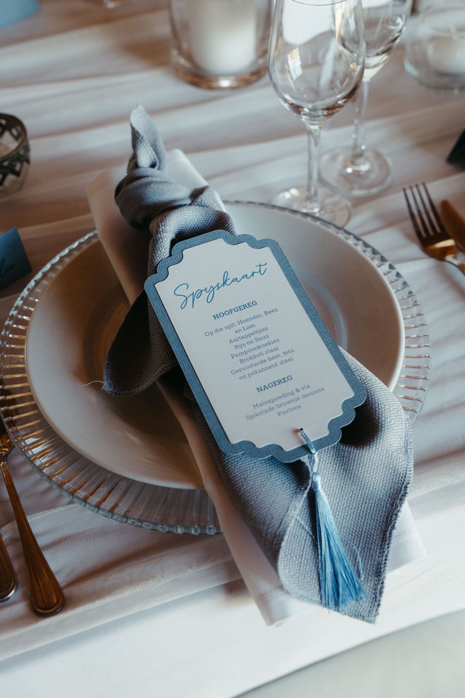Elegant wedding table setting with light blue napkins and menu cards on white plates with silver charger plates.