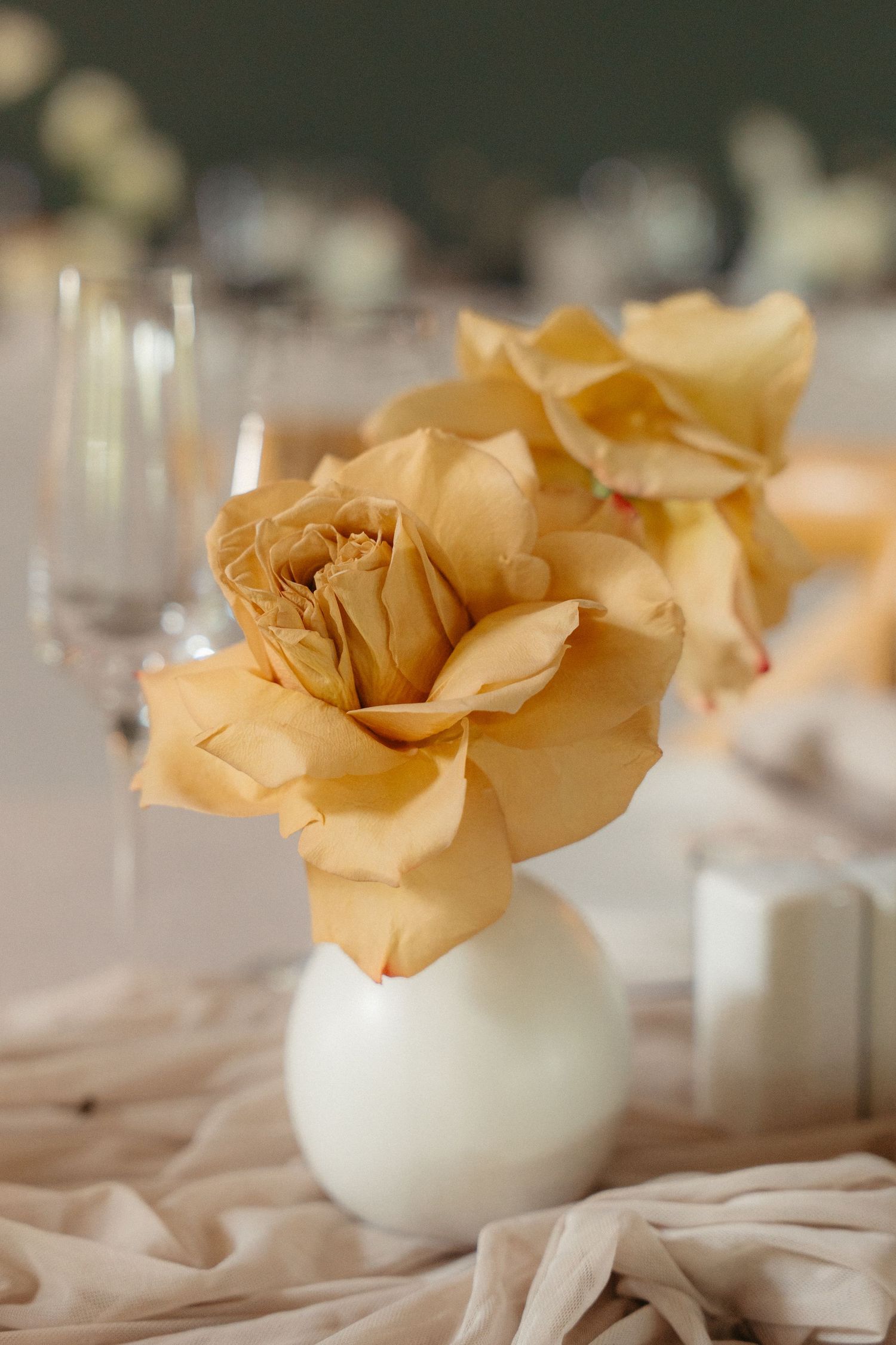 A series of delicate peach-colored paper roses arranged in small white vases on an elegant table setting.