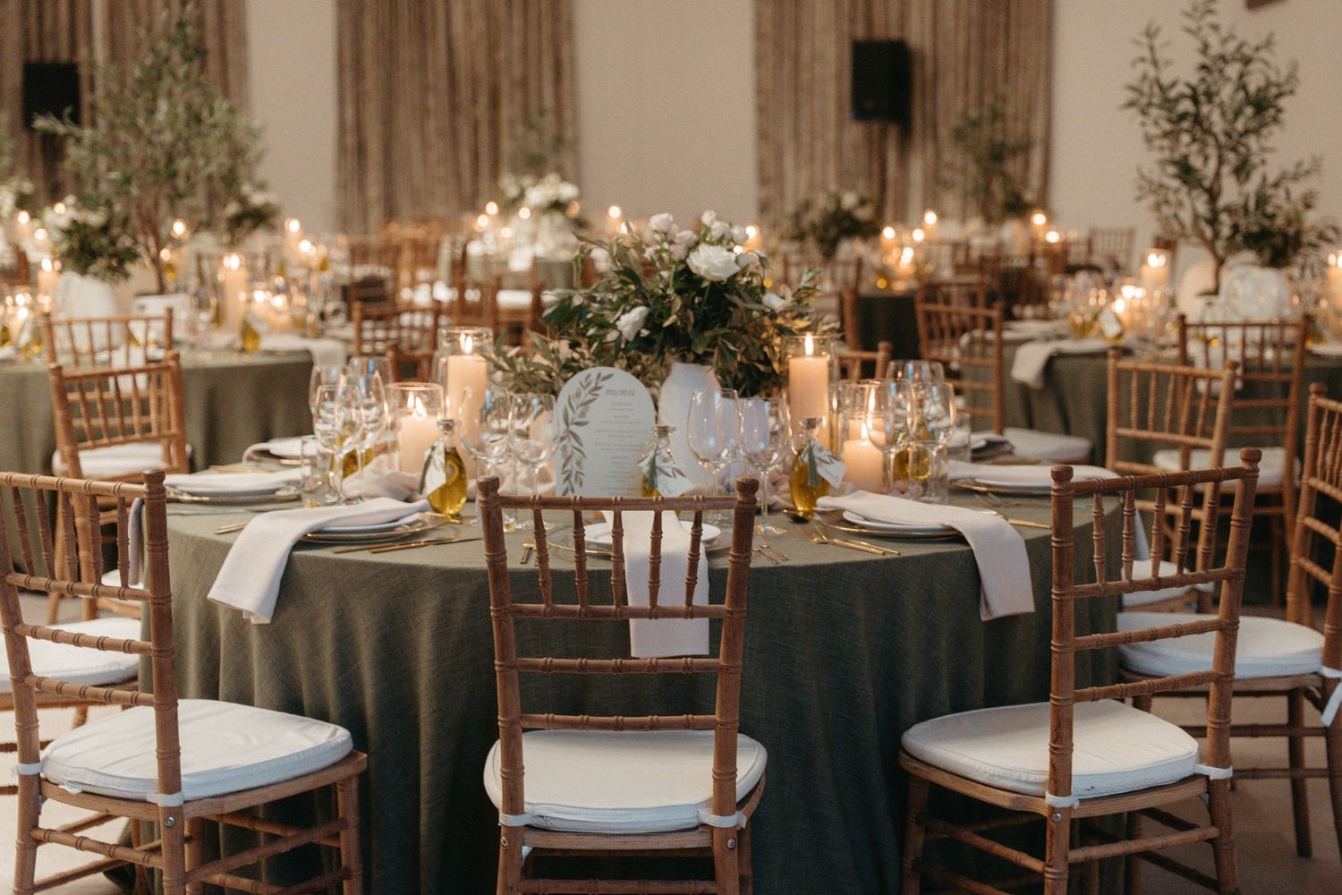 Elegant wedding reception with gold chiavari chairs, olive green tablecloths, candlelit centerpieces, and lush floral arrangements.