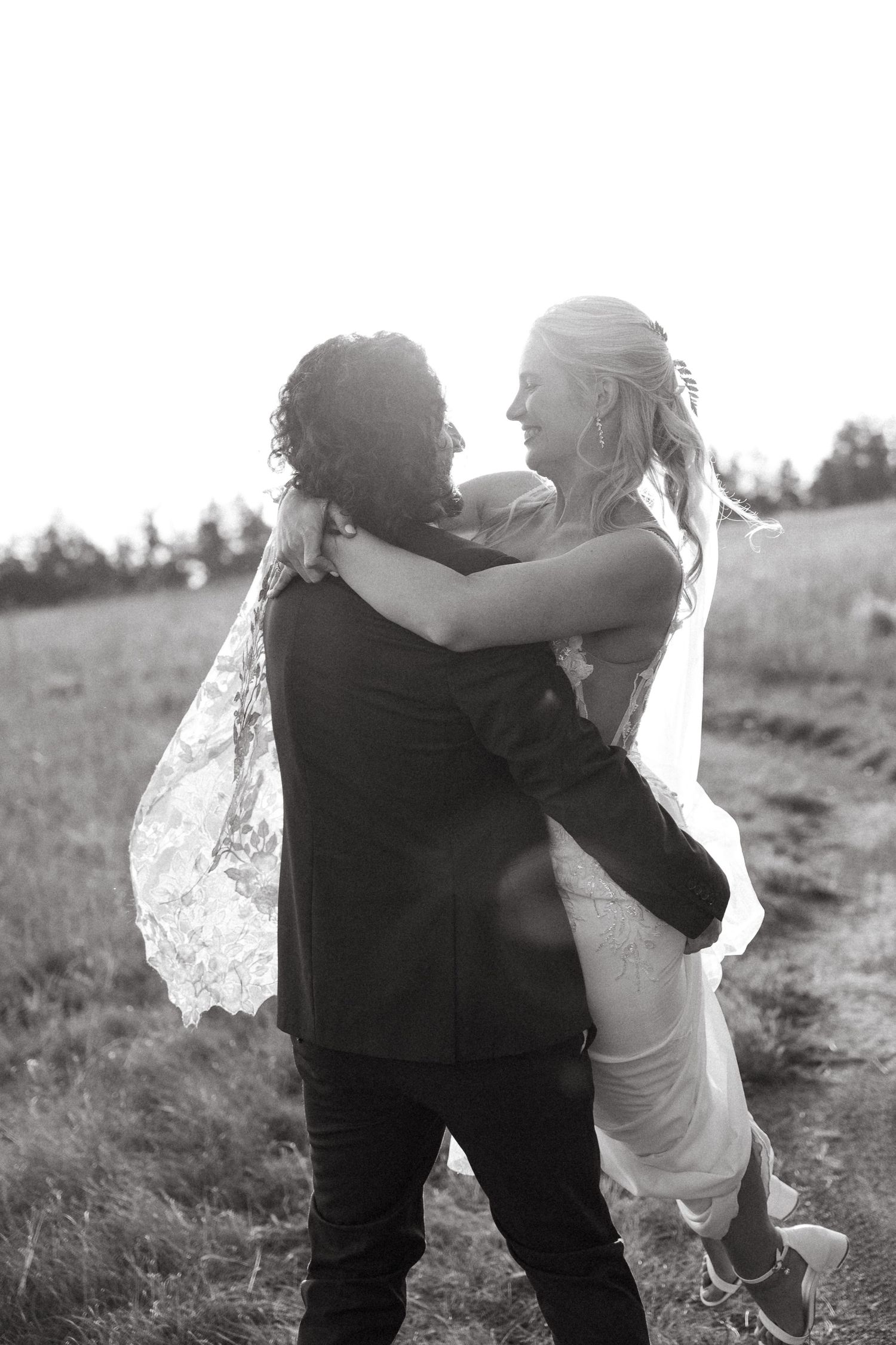 Black and white photo of groom lifting bride in a field, sharing a romantic moment on their wedding day.