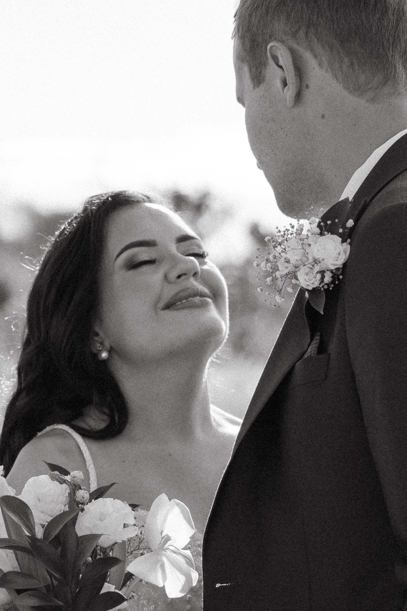 Black and white wedding photo of bride with bouquet gazing up at groom in suit with boutonniere.