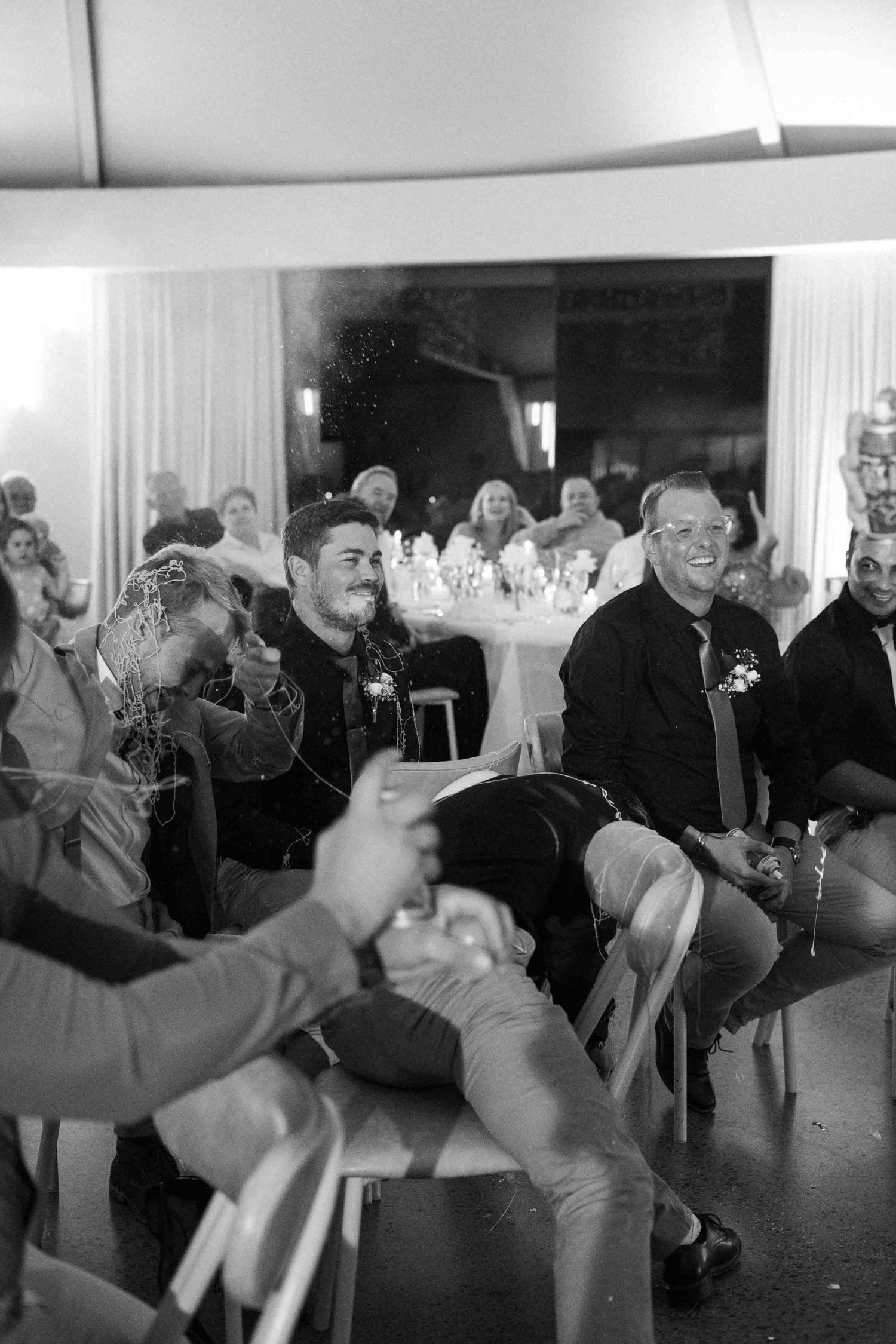 Black and white photo of smiling wedding guests seated at a reception celebration with streamers flying.