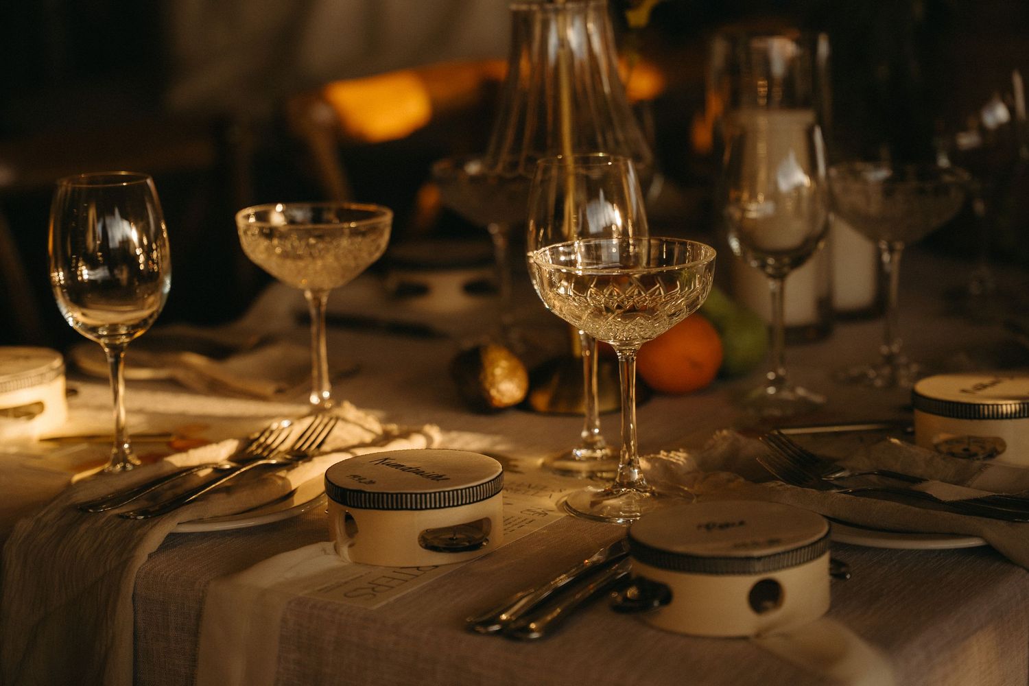 Elegant candlelit wedding decor setting with crystal glasses, gold cutlery, and fine china on a linen tablecloth.