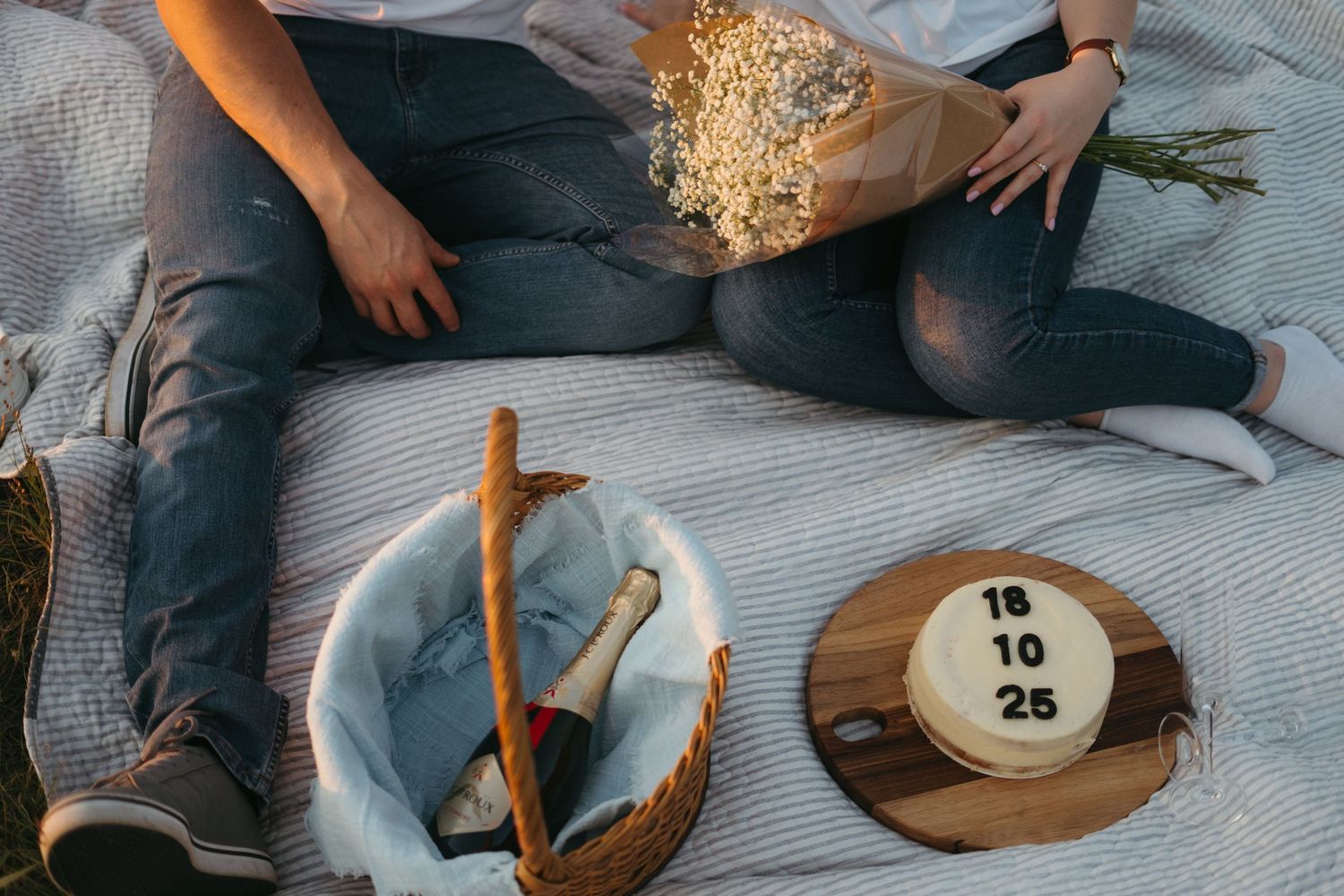 Casual picnic setup on picnic blanket with cake with wedding date, flowers and champagne