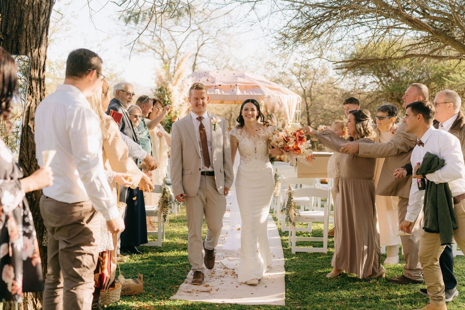 Bride and groom walk down garden aisle in Polokwane, Limpopo as guests toss petals during outdoor wedding ceremony.