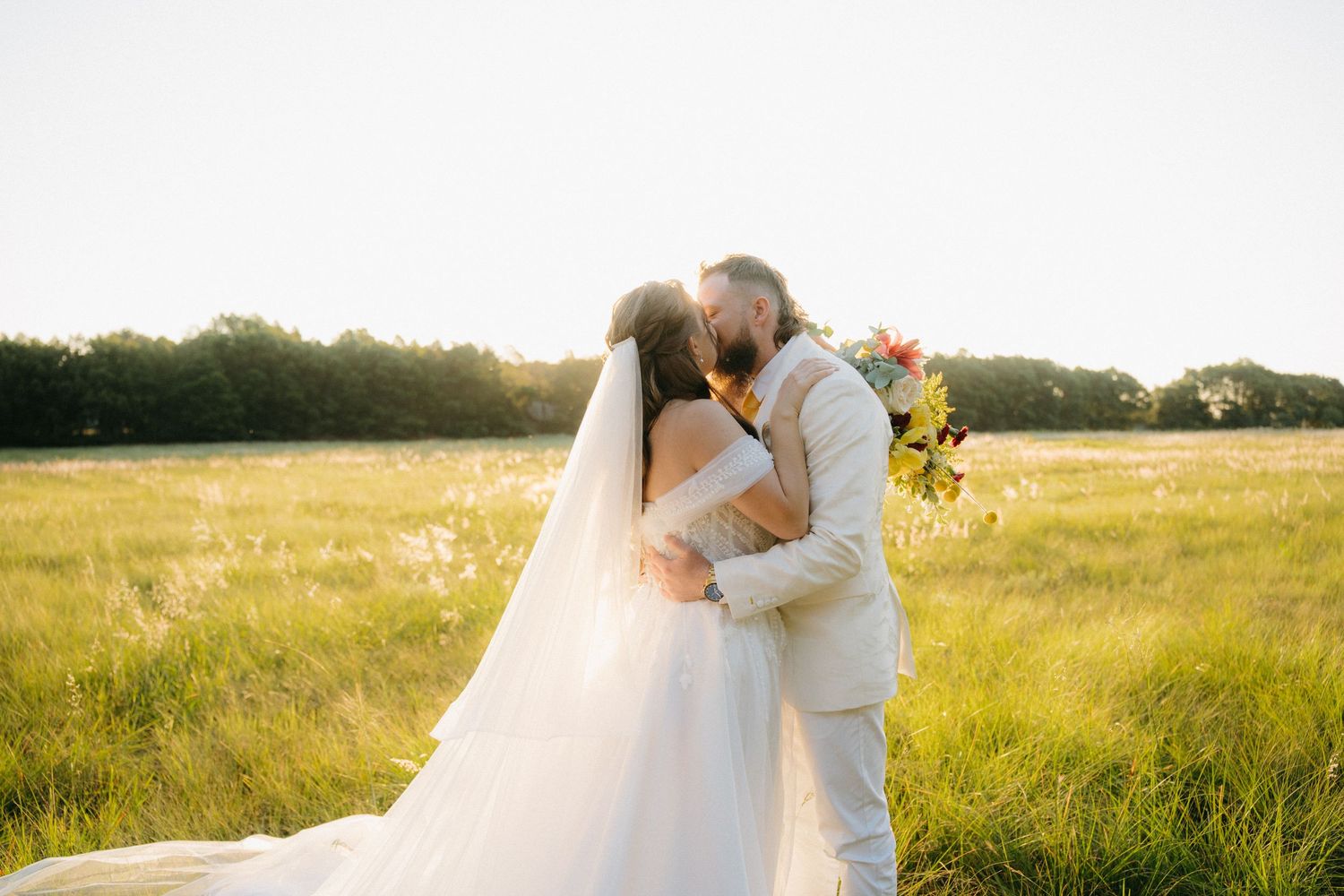 Romantic sunset wedding portrait in a golden meadow with flowing white dress and flowers.