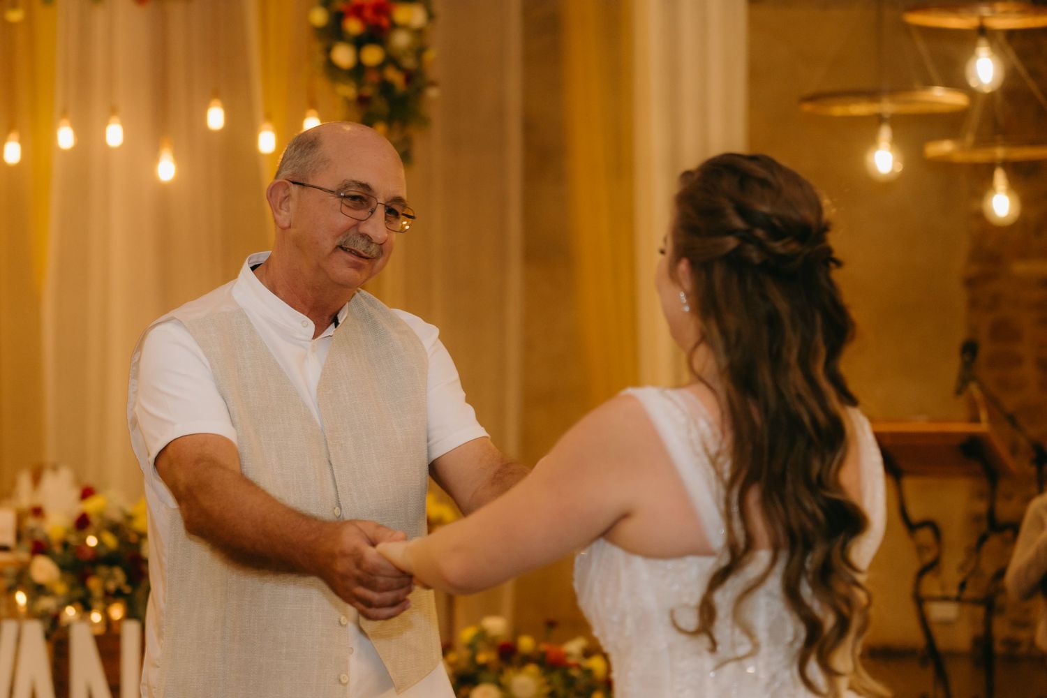 Couples first dance under warm lighting at indoor wedding reception.