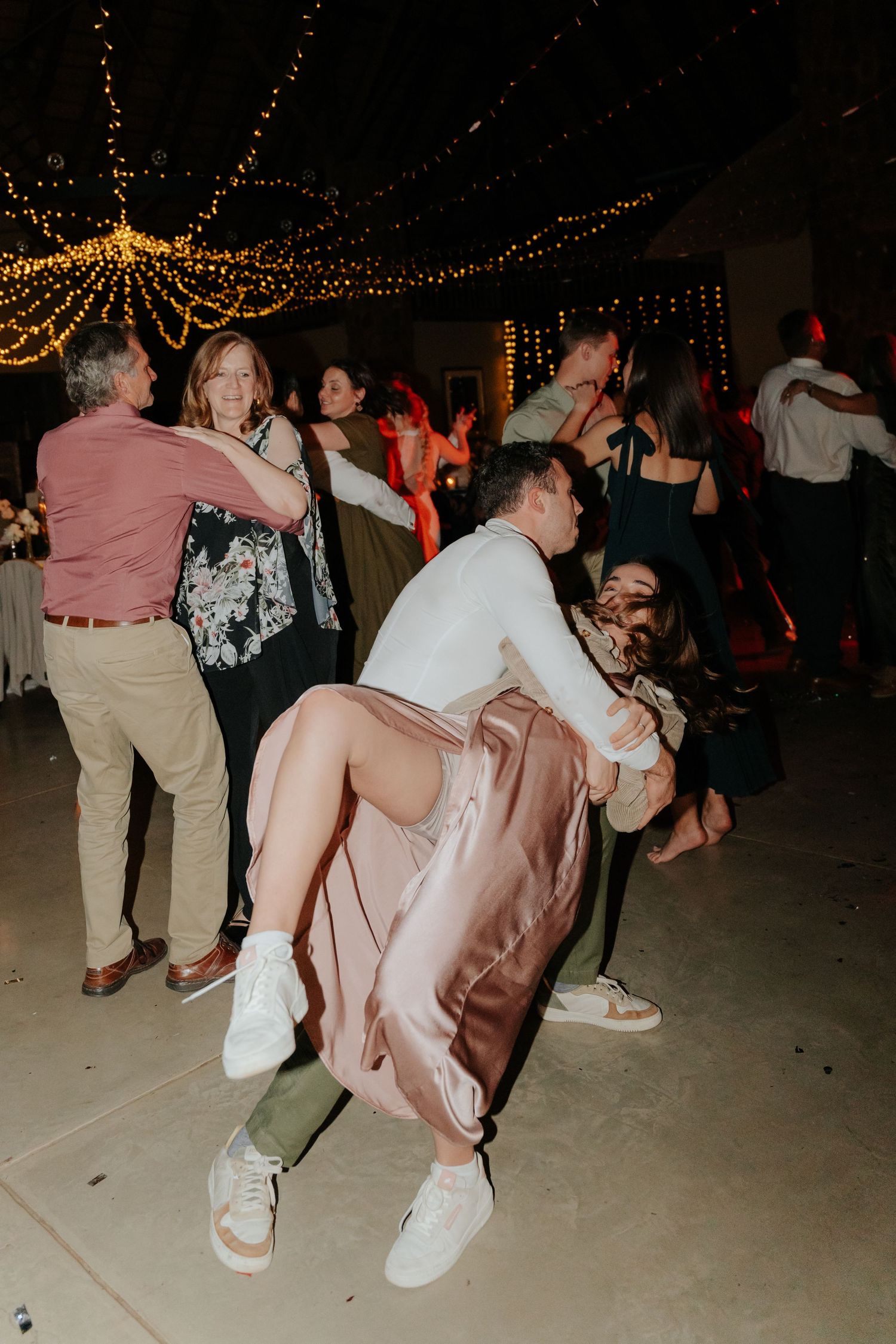 People dancing and having fun at a wedding reception under string lights.