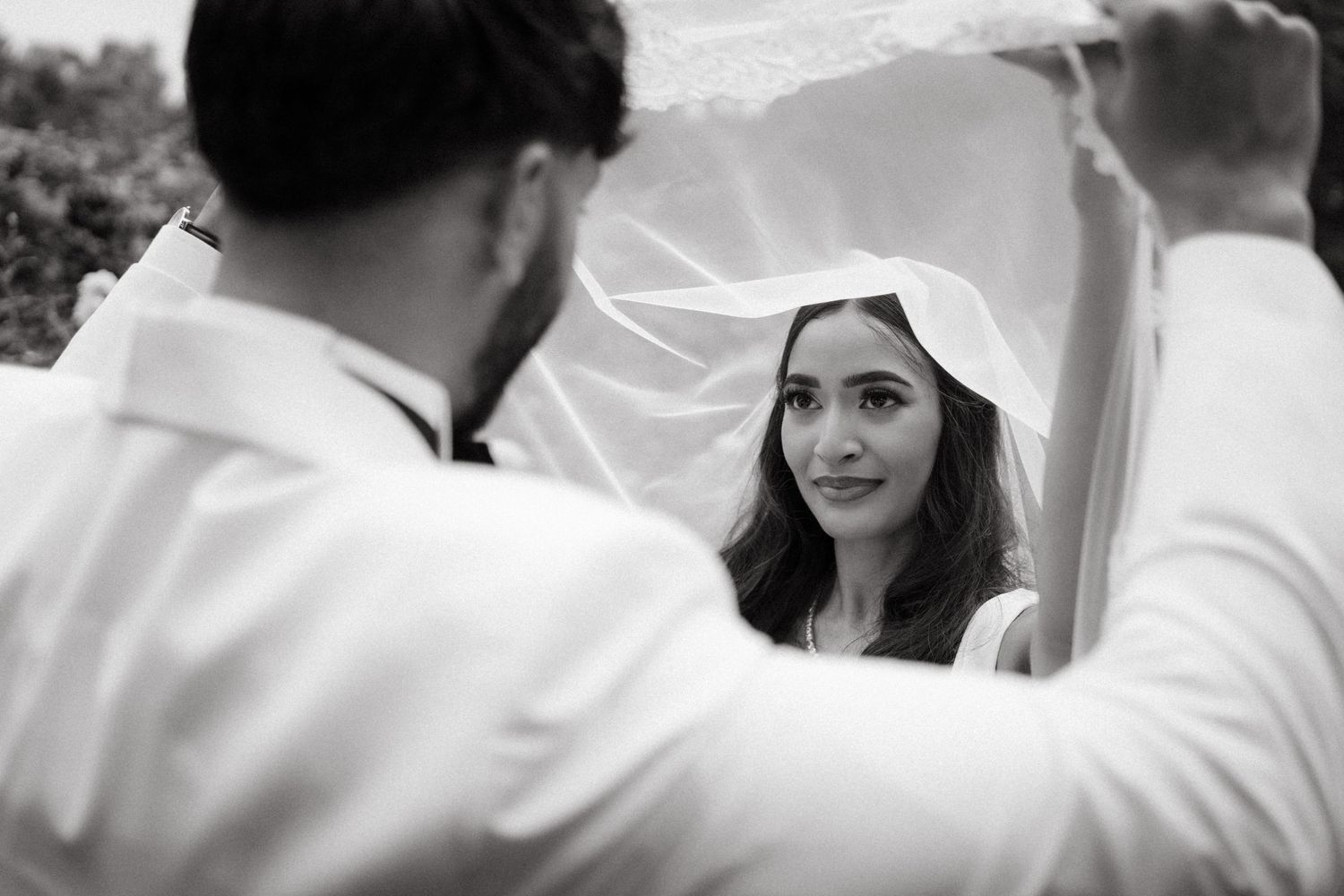 Black and white photo of a bride looking through her white veil during an intimate wedding moment.