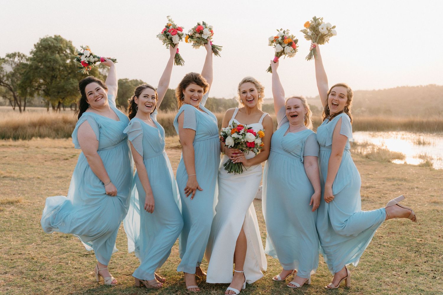 Bridesmaids in matching blue dresses pose together outdoors during golden hour.