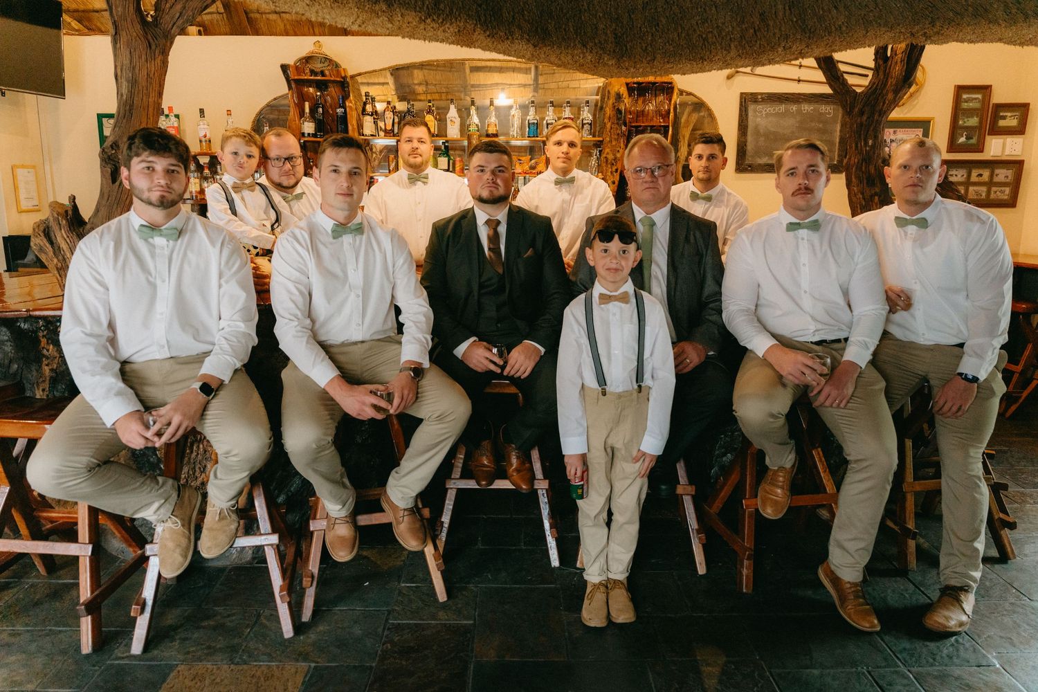 Wedding party members in casual attire sit together for relaxed group photo.
