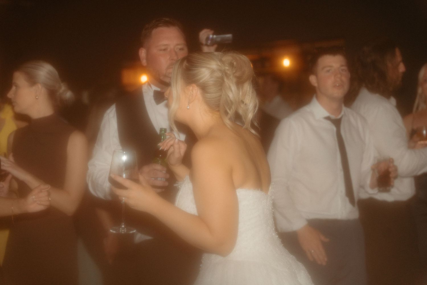 Couples dancing together at a dimly lit wedding reception with warm ambient lighting.
