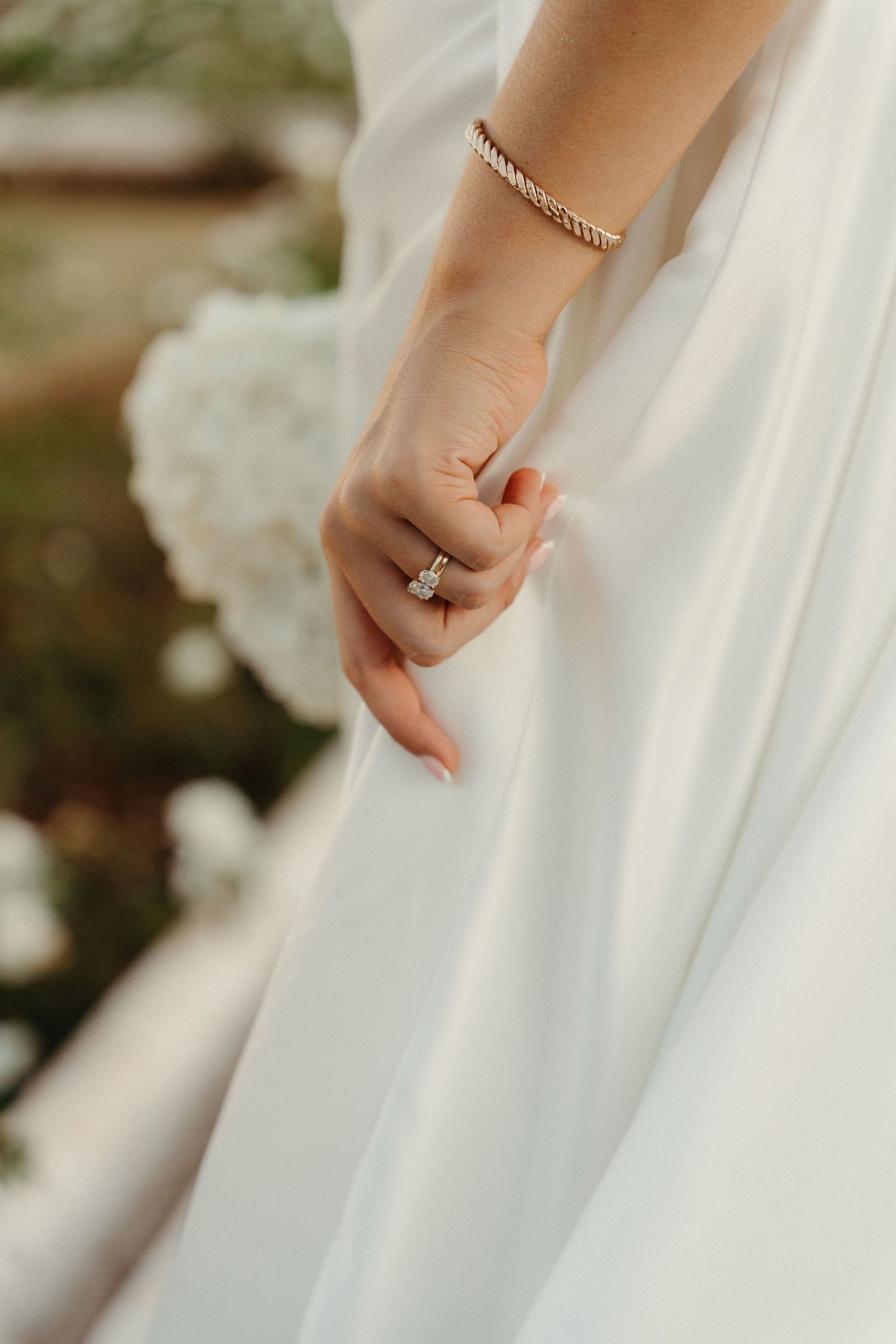 Close-up detail shots of hands delicately holding flowing white wedding dress fabric in natural light.