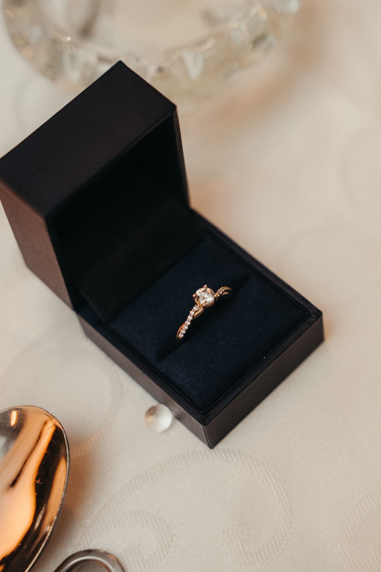 Gold diamond engagement ring in a black velvet jewelry box on a white surface.