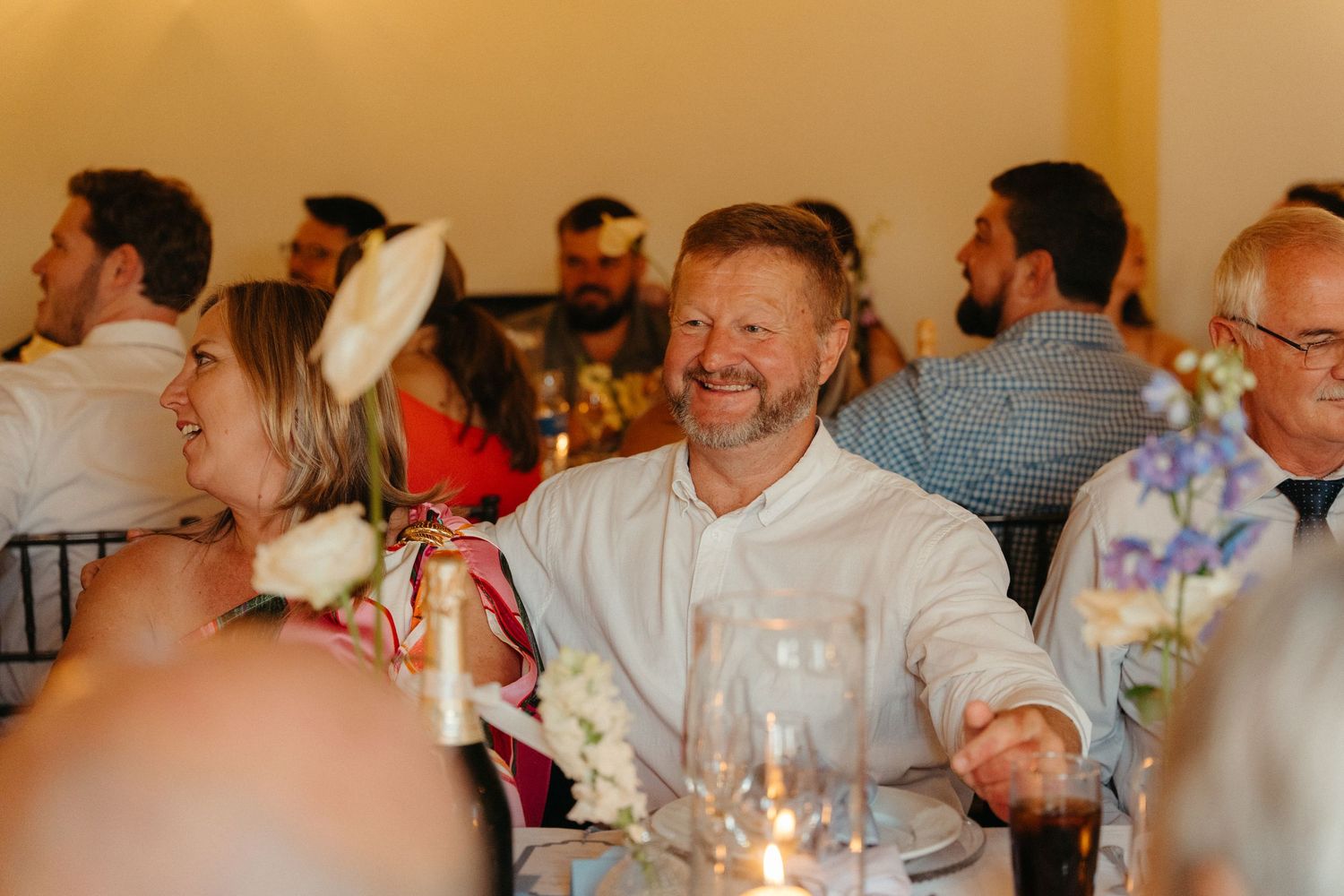 A group of people gathered around tables at a social event with candlelight and festive decorations.