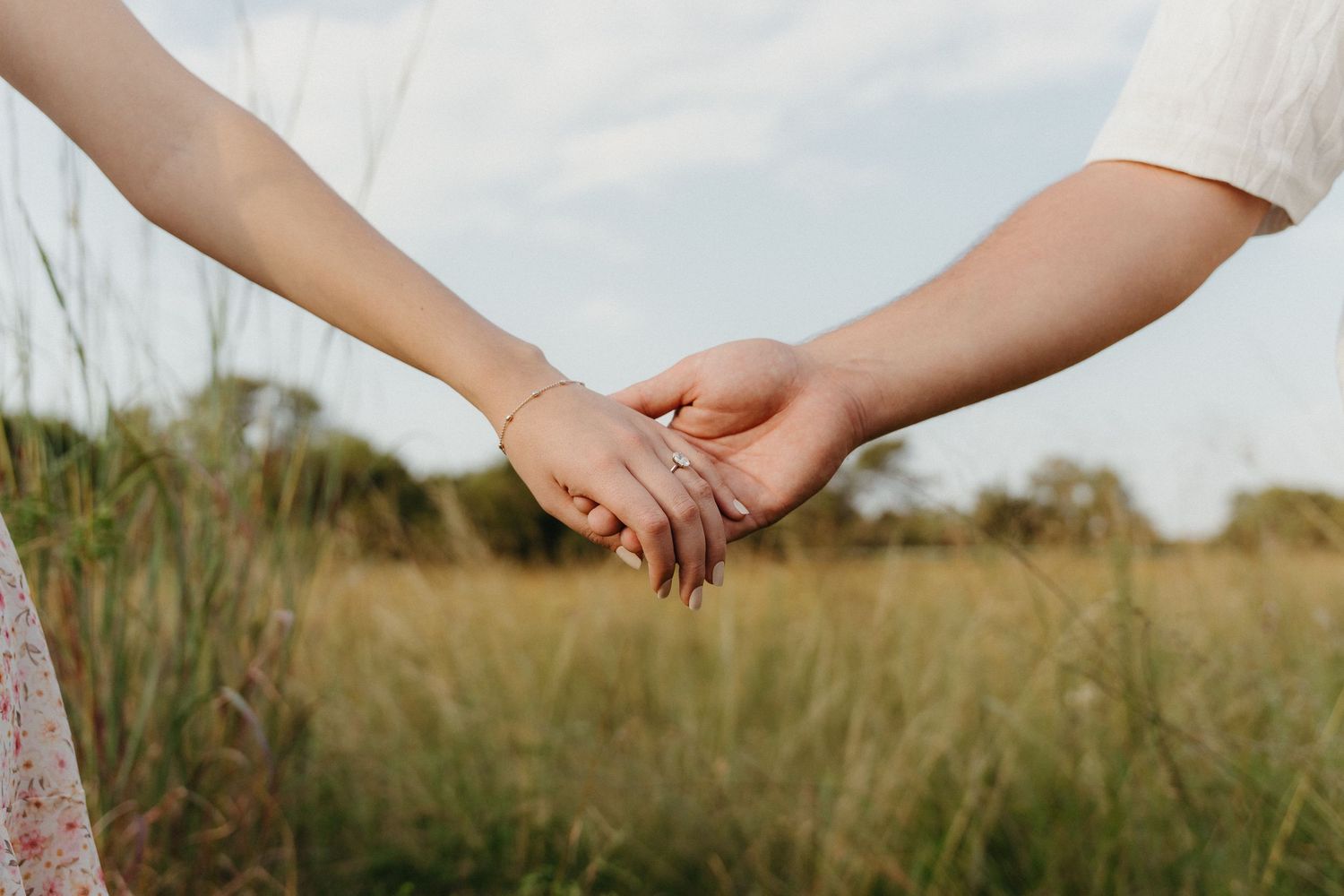 Two people holding hands in a field of tall grass, symbolizing love and connection outdoors.