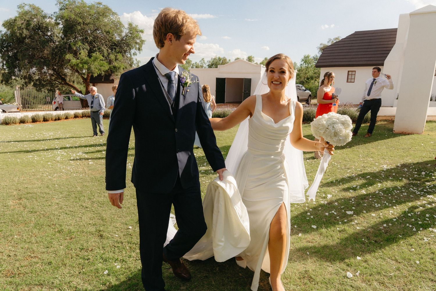 Newlywed couple shares romantic moments on a sunny day in a grassy outdoor setting during their wedding celebration.