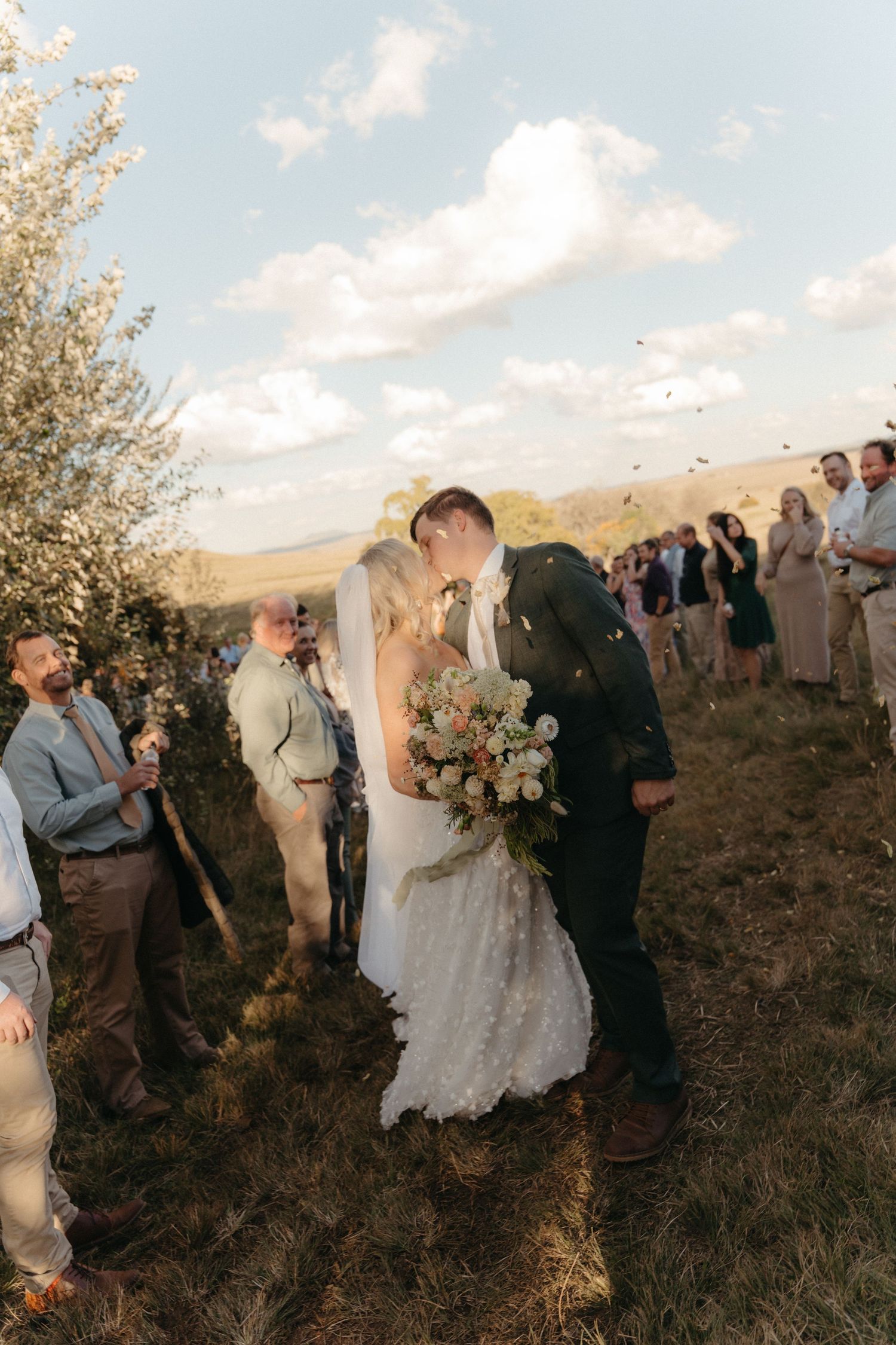 Newlyweds kissing during outdoor ceremony as guests toss confetti at sunset in the Free State
