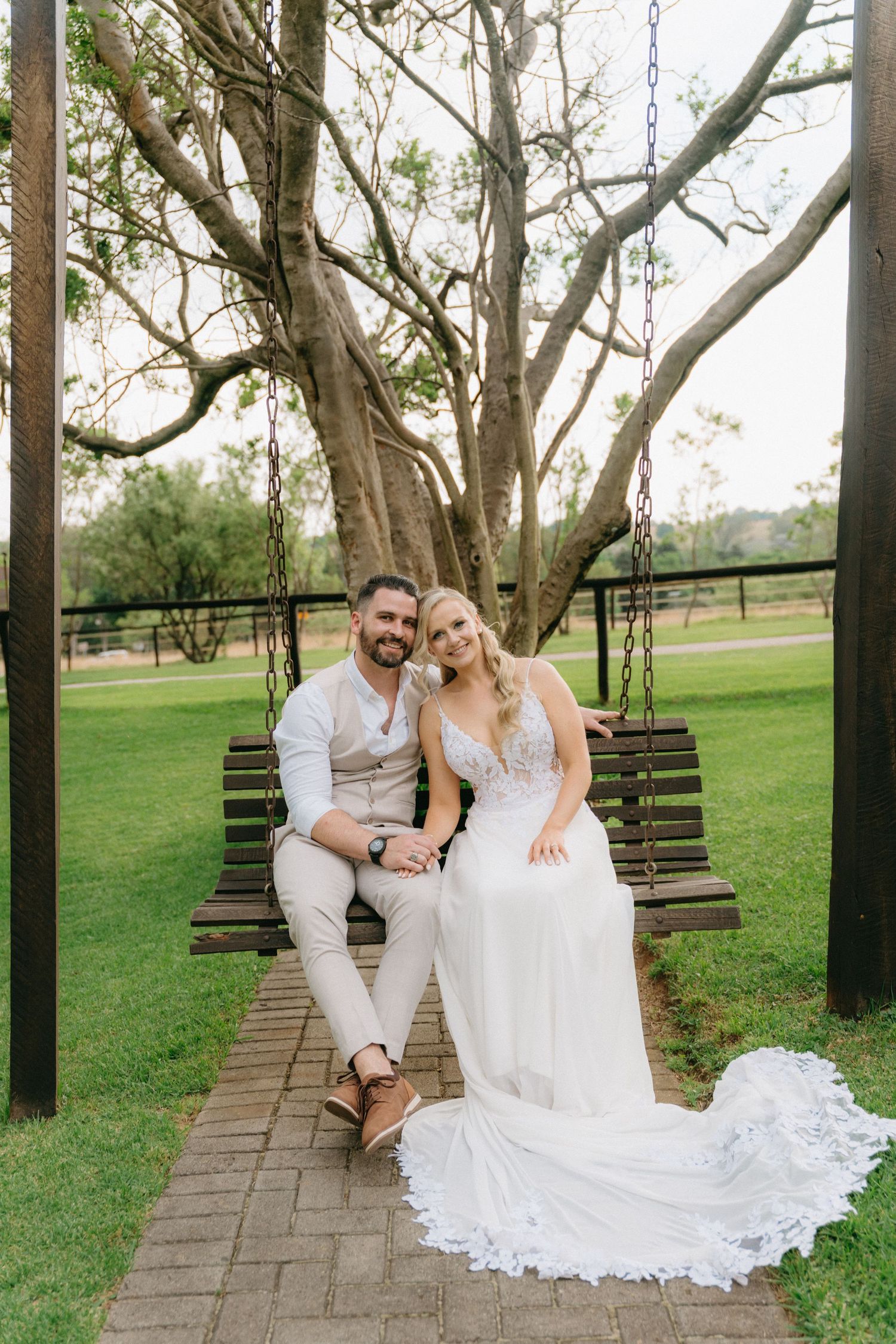 A couple sits together on wooden swings in a scenic outdoor park setting.