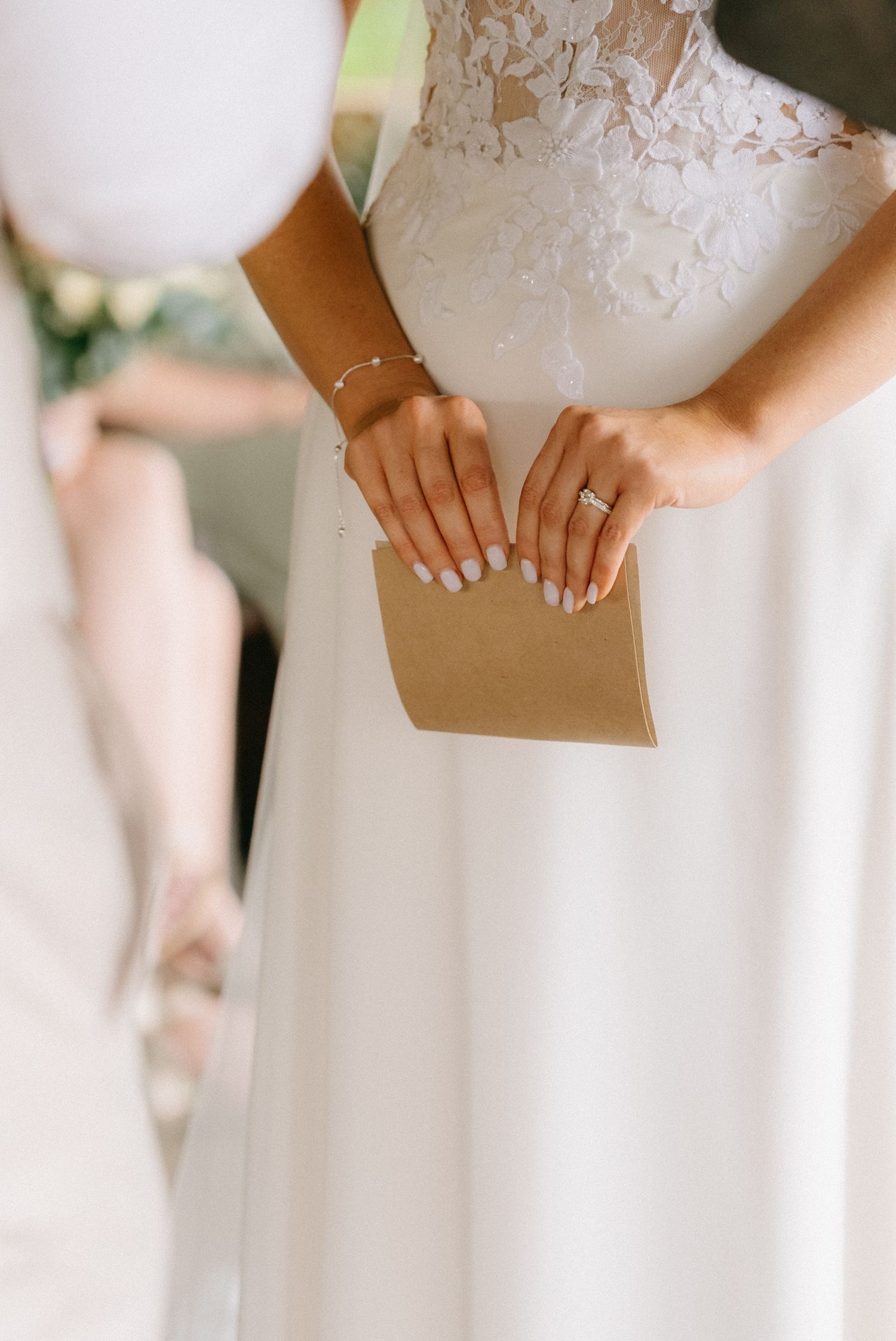 Close-up view of hands holding a brown paper envelope against a white dress.