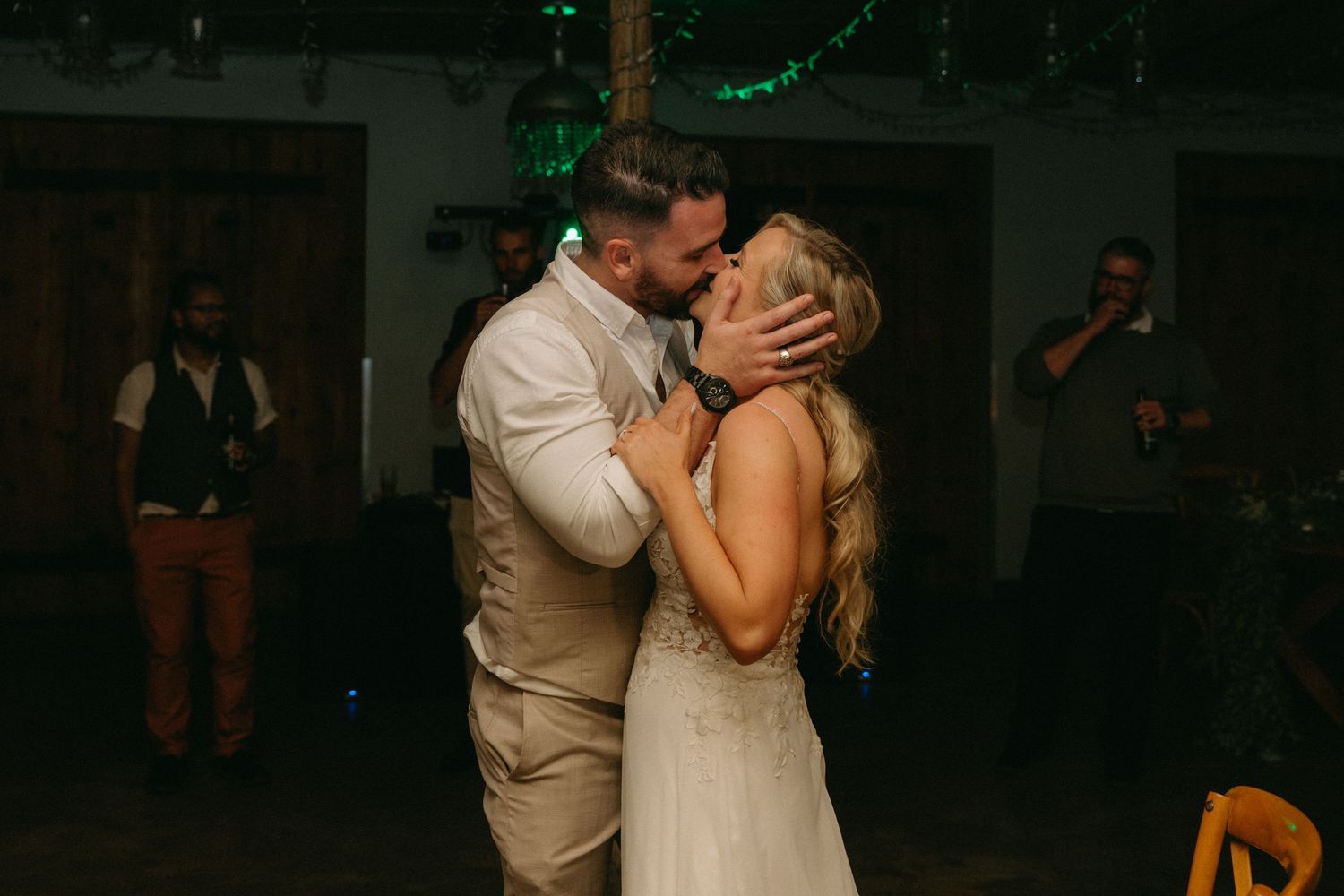 A couple shares a romantic dance moment at a dimly lit wedding reception venue with green lights in the background.