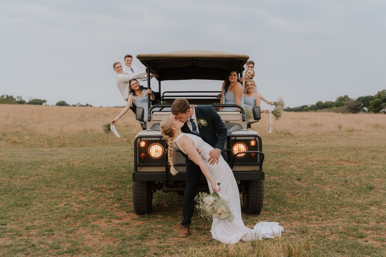 A romantic wedding photo series showing a couple posing with a vintage Land Rover Defender in a rustic field setting.