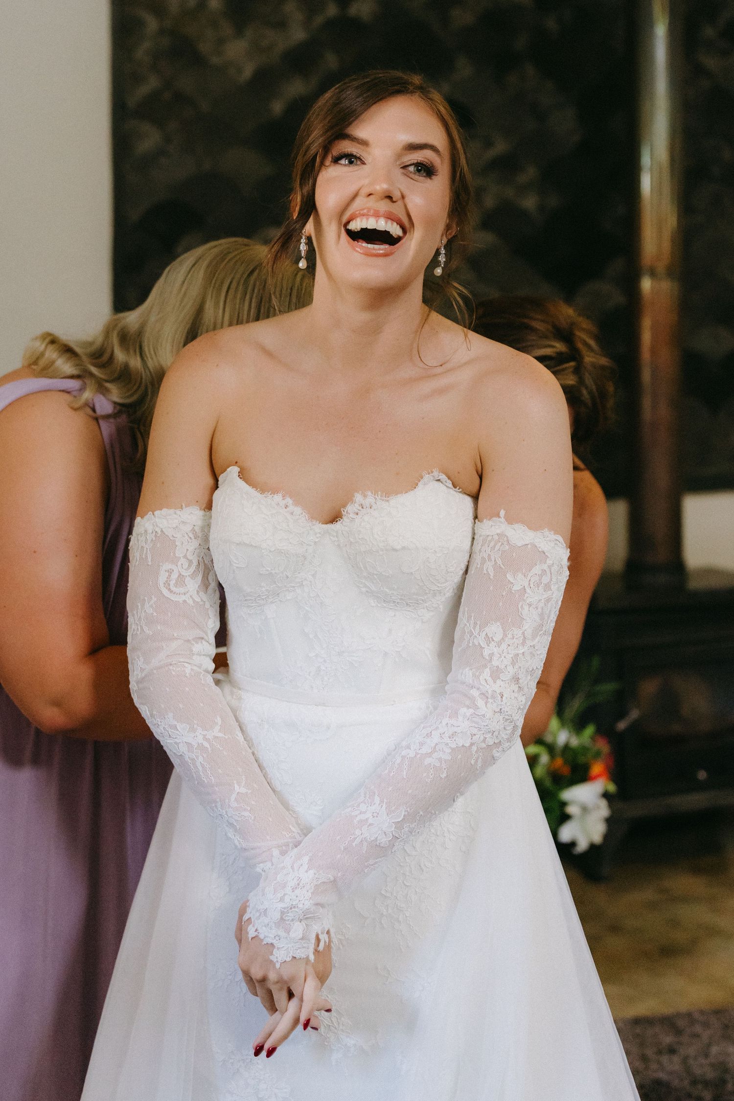 A joyful moment captured of a bride wearing a white lace wedding gown with off-shoulder long sleeves.