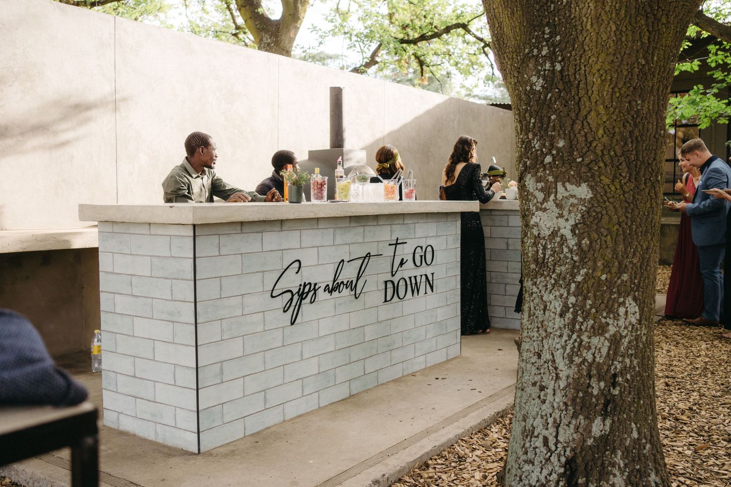 A modern white brick bar setup outdoors under trees serves guests at an outdoor event.