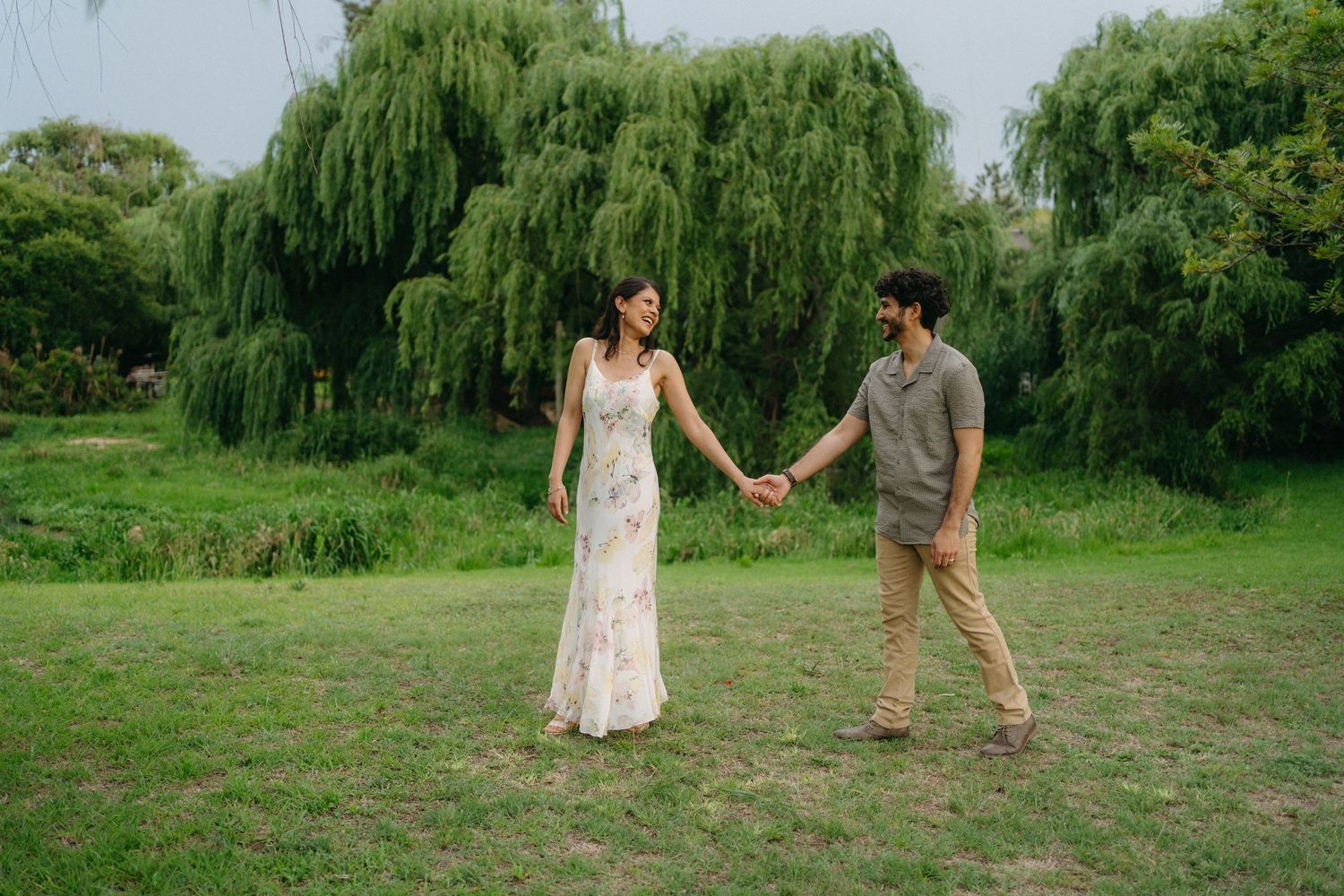 A couple holding hands while walking through tall grass at dusk.