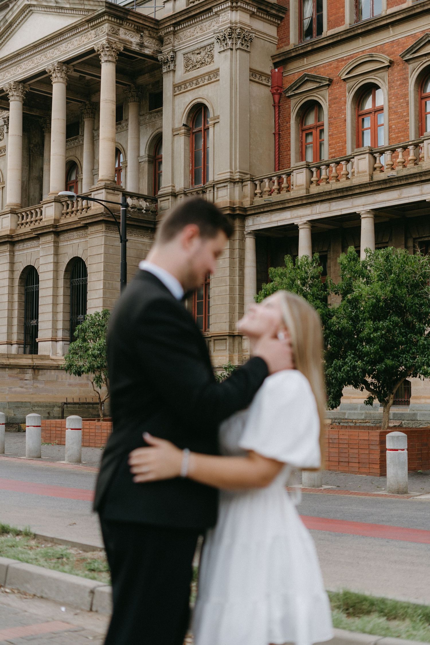 A romantic moment outside a historic building with classical architecture and tall white columns.