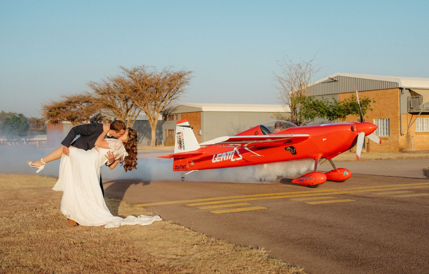 A dramatic wedding photo with a red vintage airplane and smoke effects on an airfield.