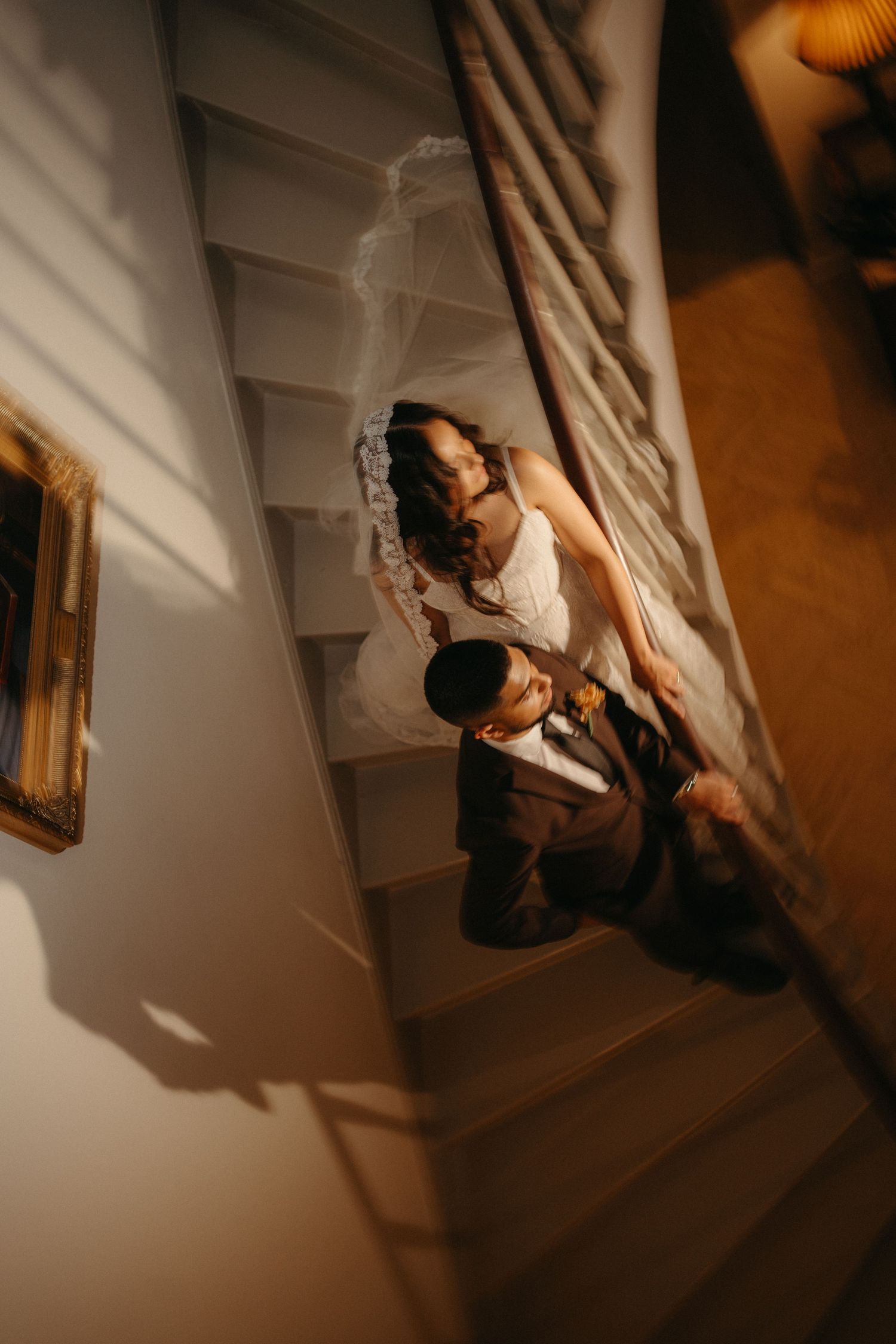 Aerial view of a bride and groom walking up a staircase, bride wearing a flowing veil in warm golden light.