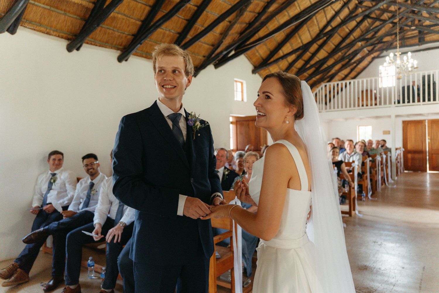 Wedding guests and couple gather in a rustic venue with exposed wooden beams and natural lighting.