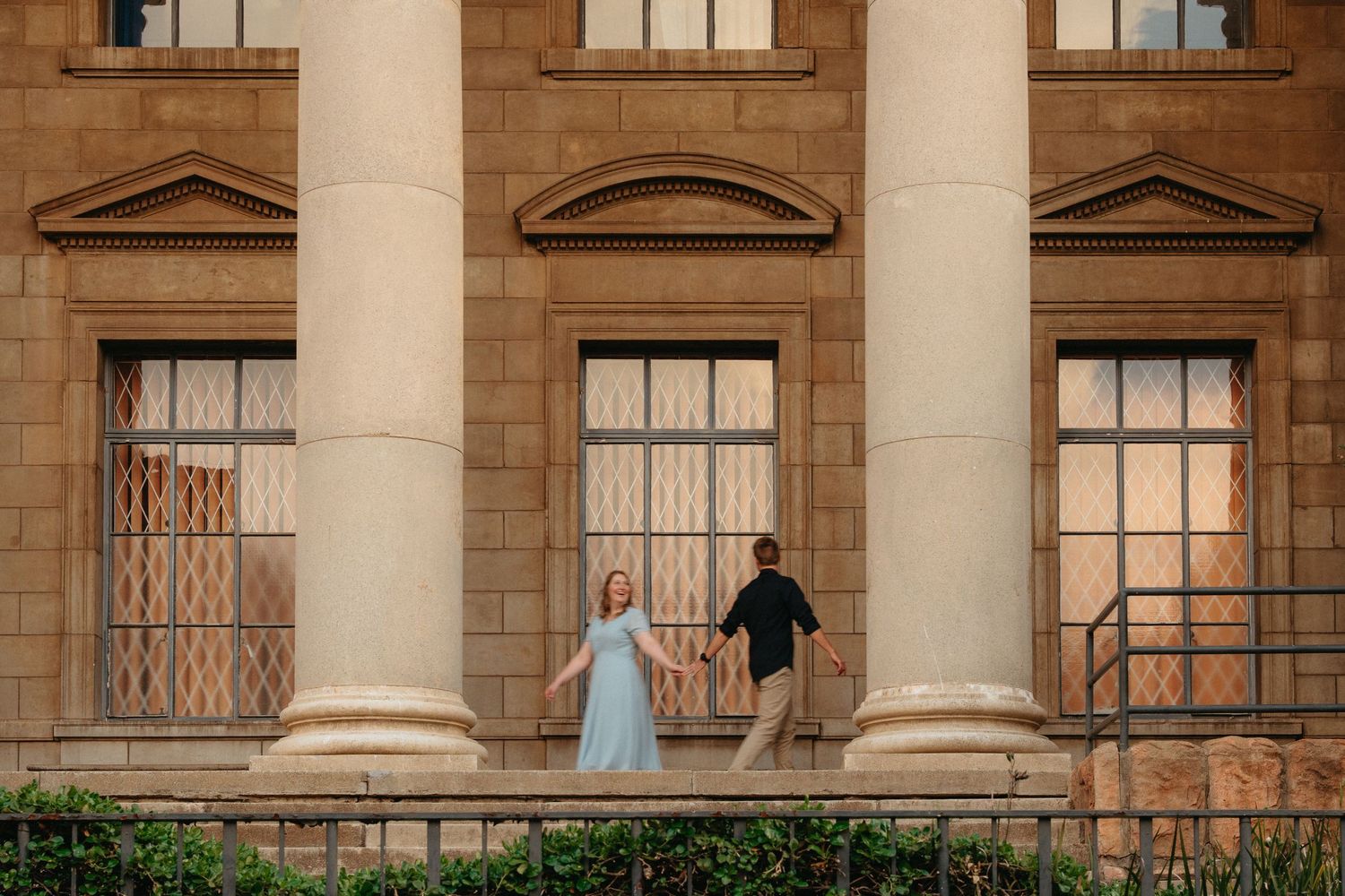 Two people stand between grand white columns on a historic building's porch at sunset.