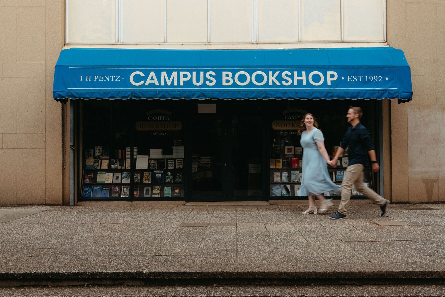 A blue awning marks the entrance to a Campus Bookshop with bookshelves visible through the storefront window.