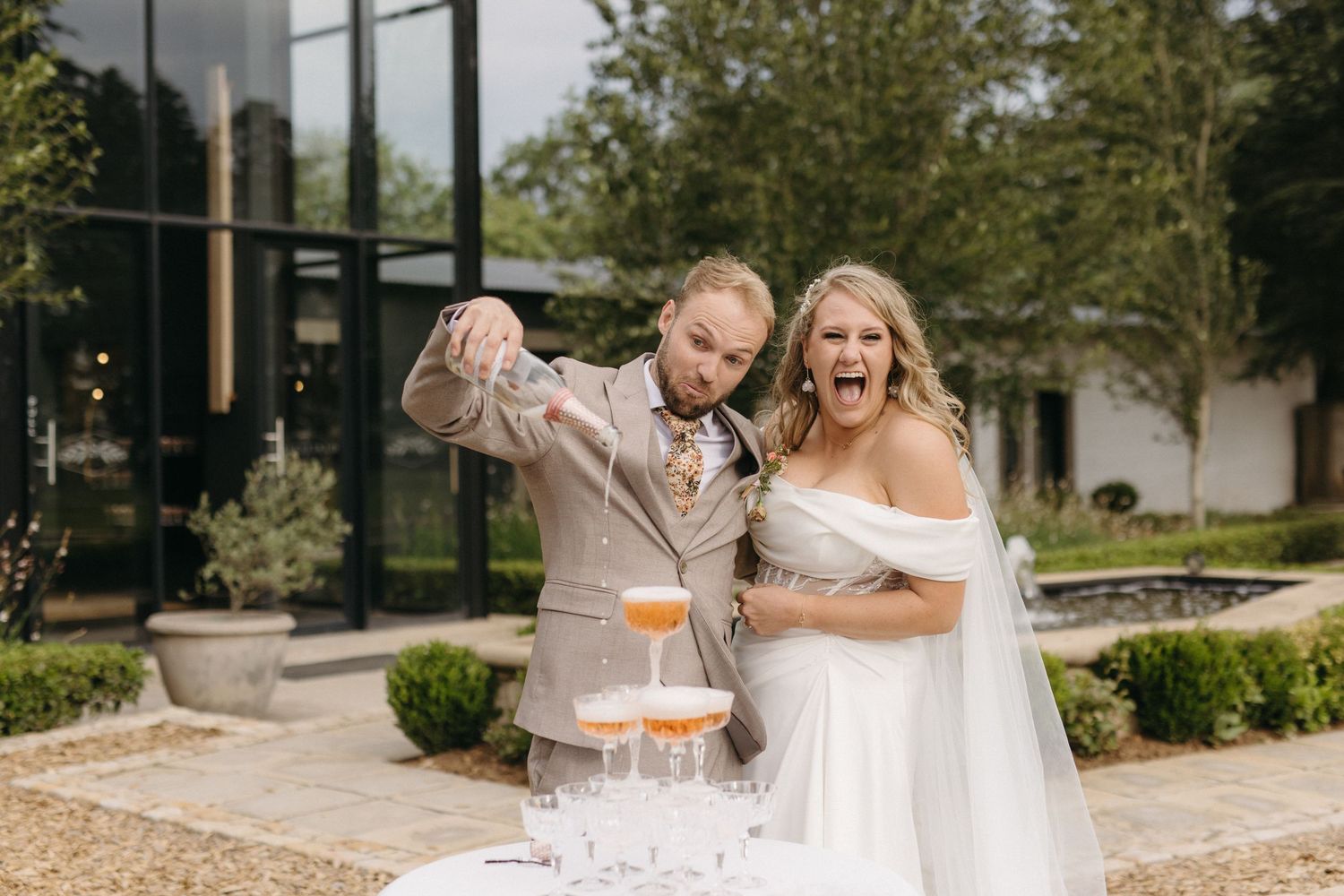 Excited bride and groom pouring champagne into a tower of glasses at Smitsfield Wedding Venue